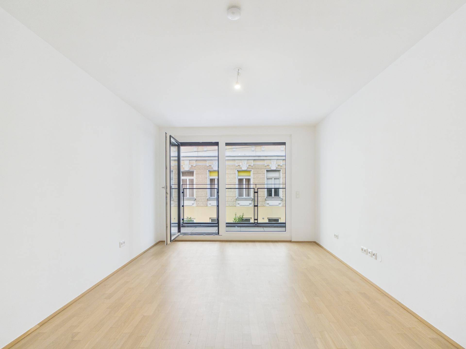 Heller Wohnraum mit Parkettboden und großen Fenstern, die viel Tageslicht hereinlassen.