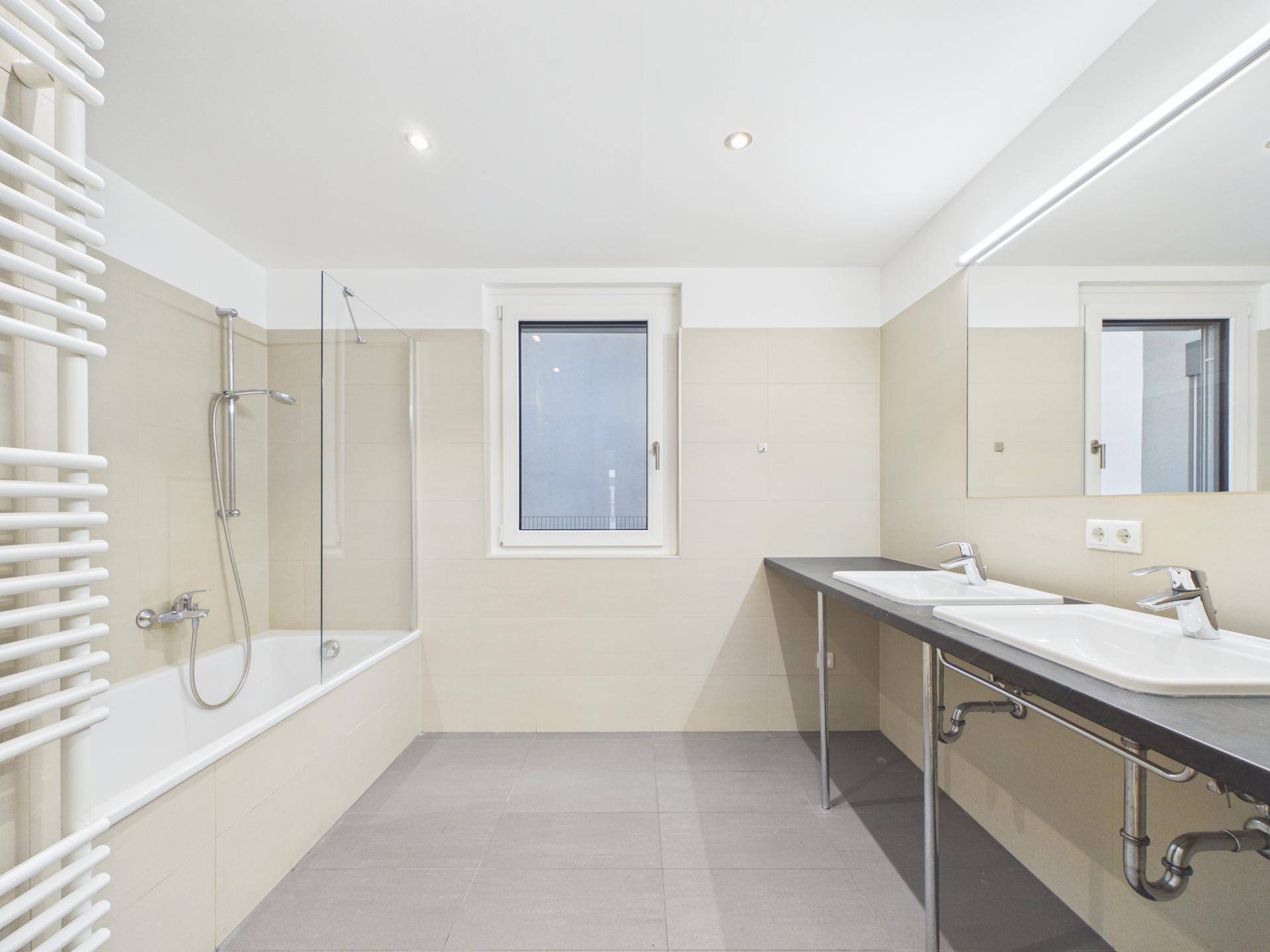 Modernes Badezimmer mit Doppelwaschbecken, Badewanne und Fenster für natürliche Belüftung.