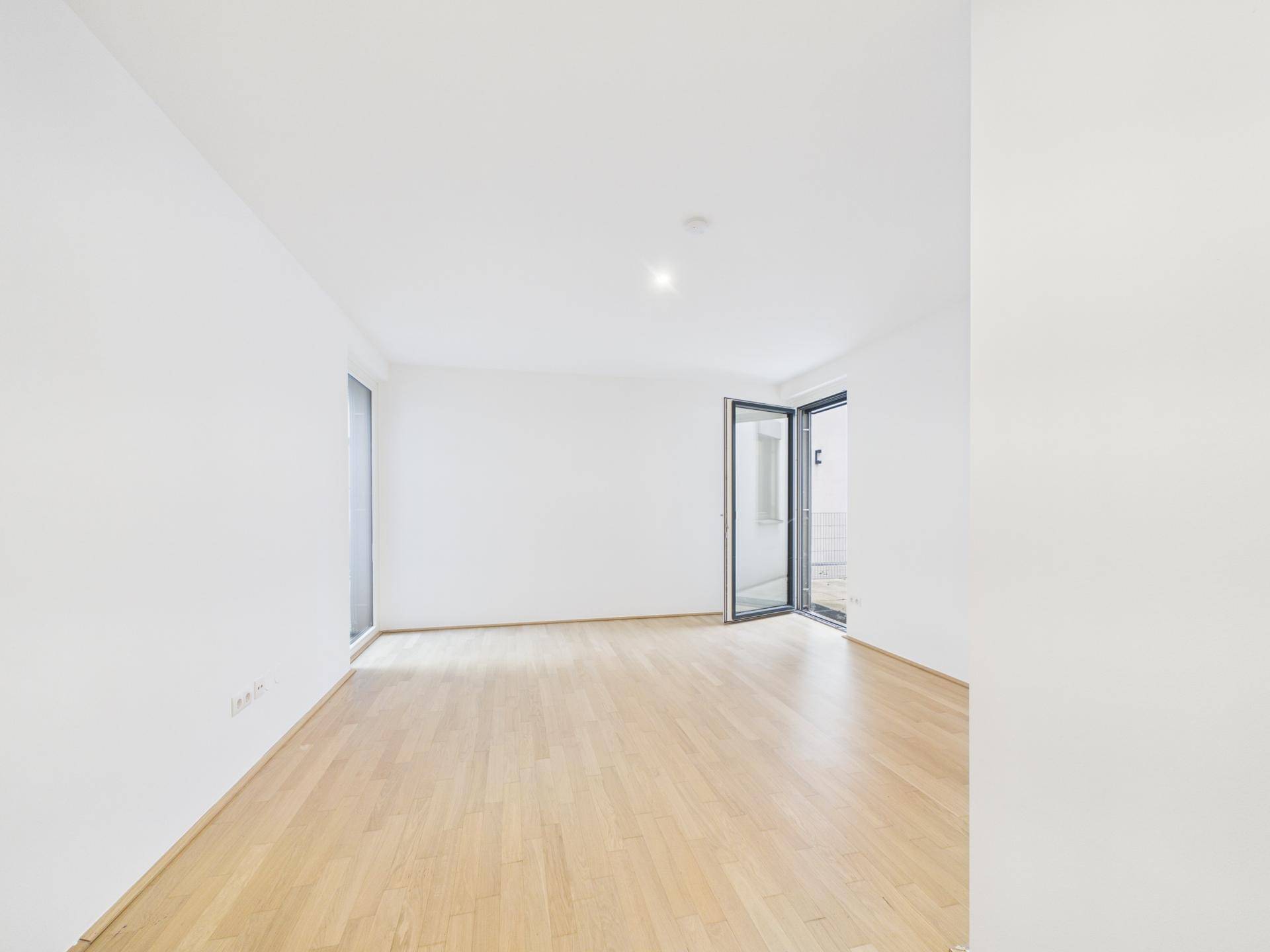 Geräumiger, heller Wohnraum mit Parkettboden und Zugang zu einem Außenbereich.