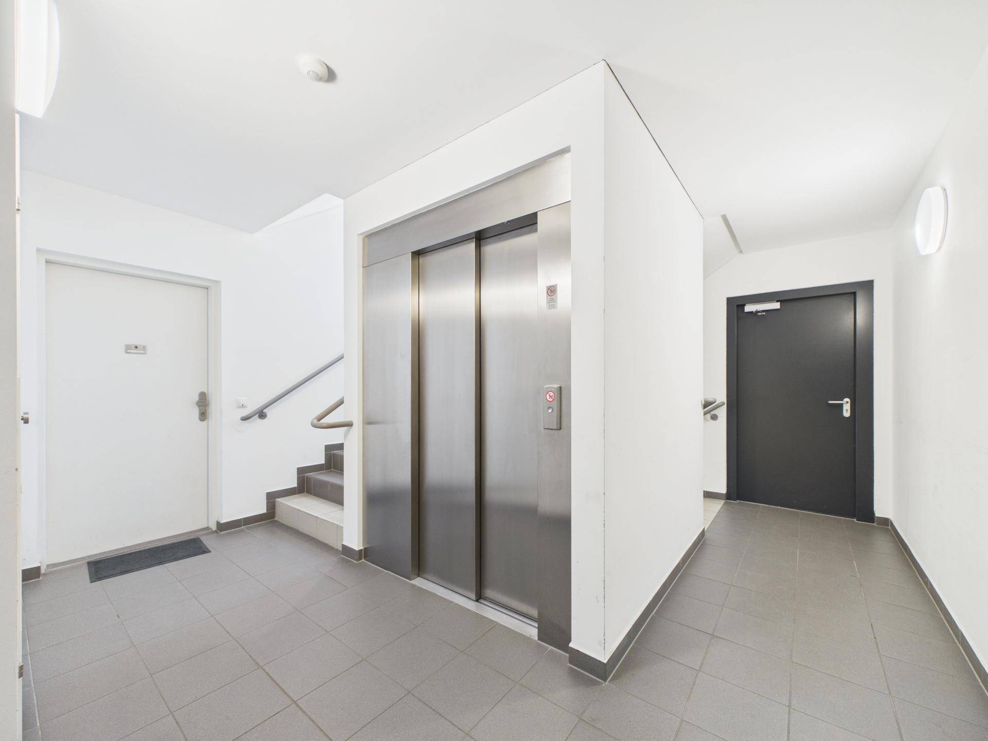 Heller Flur mit Aufzug, Treppenhaus und Fliesenboden in einem modernen Gebäude.