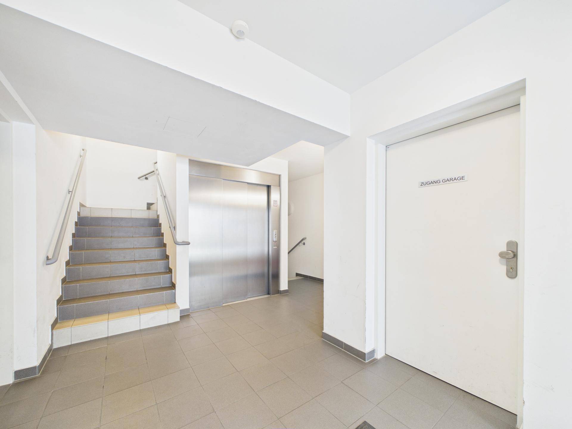 Eingangsbereich mit Aufzug, Treppe und Zugang zur Garage, alles in gutem Zustand.