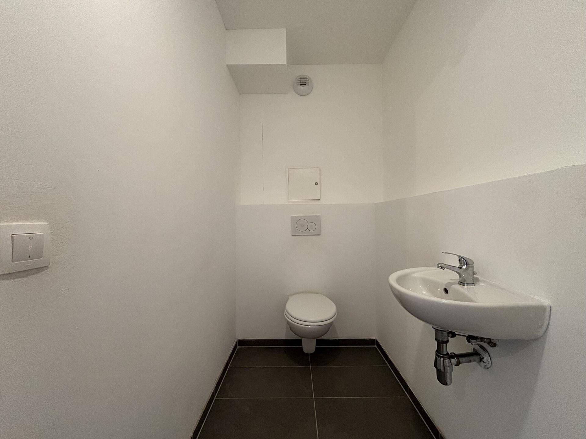 Kleines Gäste-WC mit Wand-WC, Waschbecken und dunklen Bodenfliesen, praktisch und platzsparend.