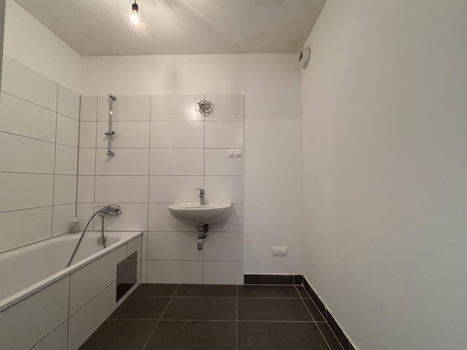 Helles Badezimmer mit Badewanne, Waschbecken und weißen Fliesen an den Wänden, funktional und sauber.
