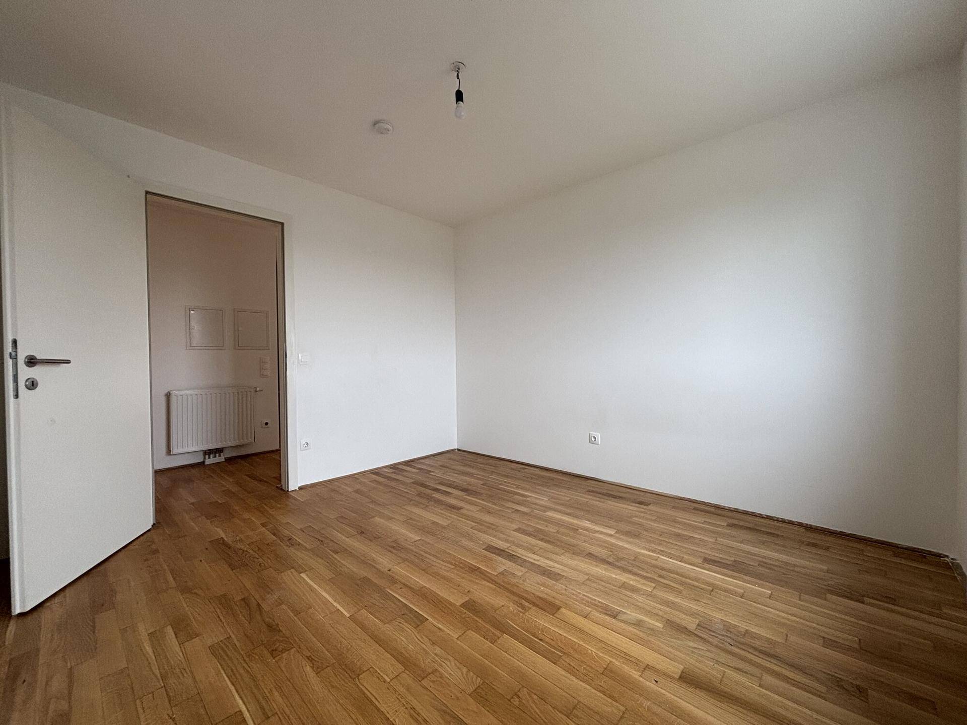 Leeres Zimmer mit hellem Holzparkett und weiß gestrichenen Wänden, bereit zur individuellen Einrichtung.