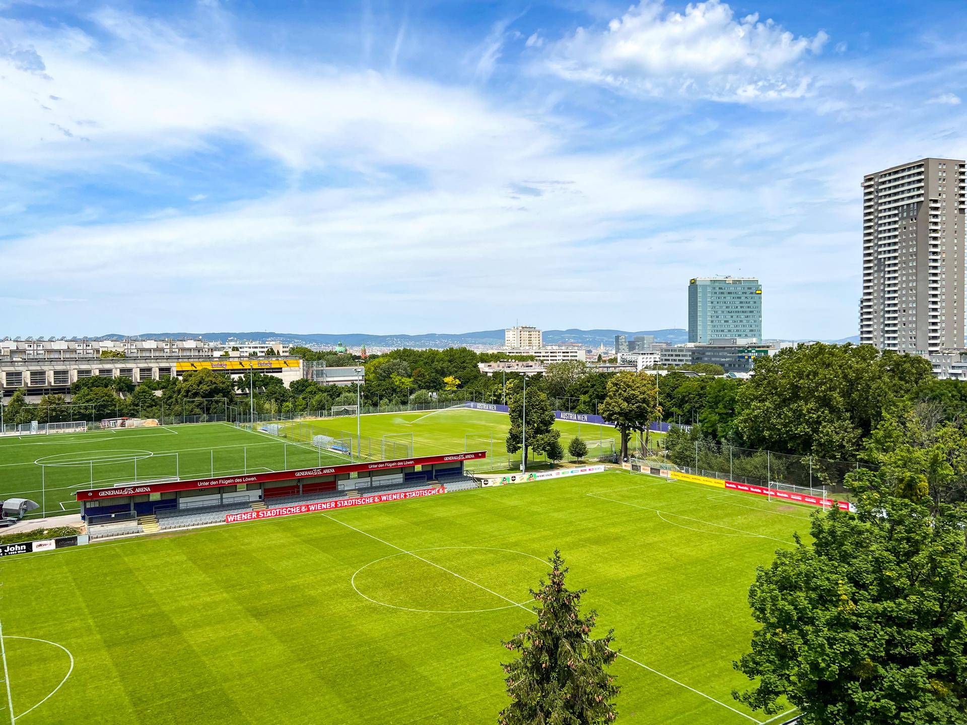 Weitläufiger Blick über Sportplätze und die Stadtlandschaft unter blauem Himmel, beeindruckende Aussicht.