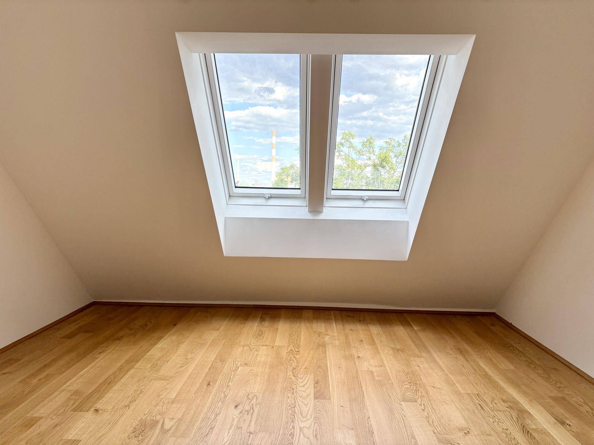 Dachzimmer mit Holzboden, Dachschräge und großem Dachfenster für viel Licht.