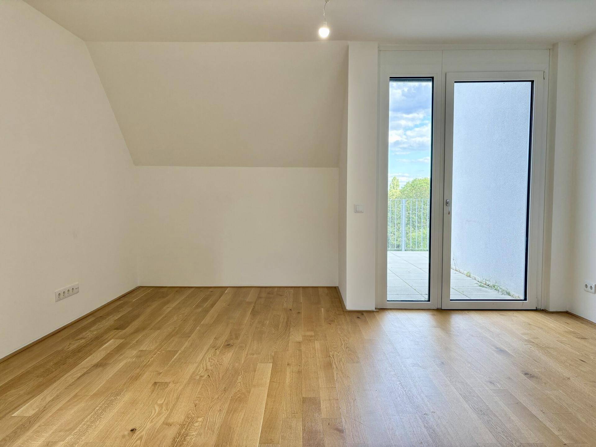 Lichtdurchfluteter Raum mit Holzboden, Dachschräge und Zugang zur Terrasse.