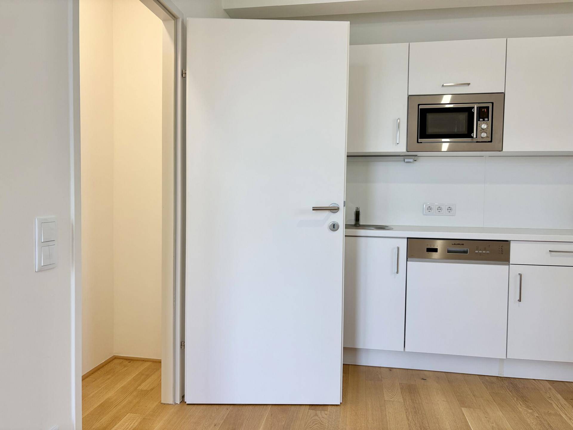 Moderne Einbauküche mit weißen Schränken, Mikrowelle, Geschirrspüler und Ofen.