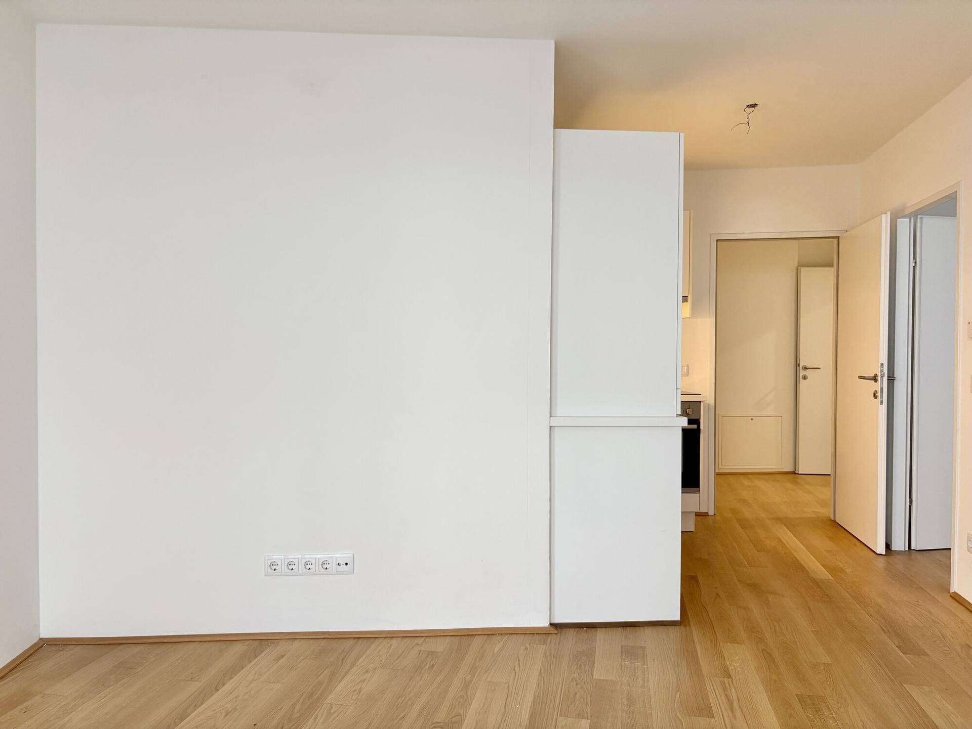 Heller Wohnbereich mit Parkettboden und integriertem Schrank, der zu weiteren Räumen führt.