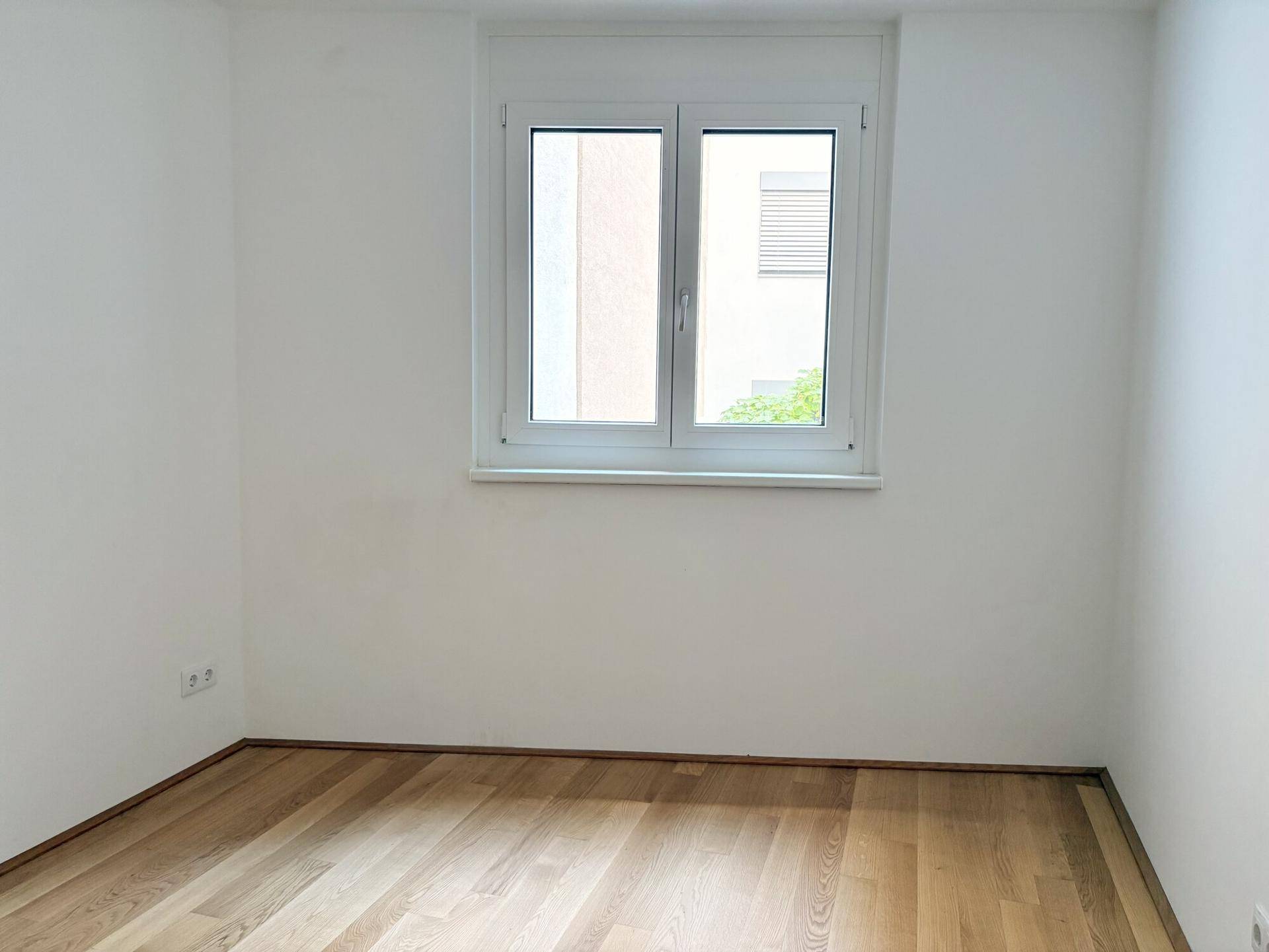 Weiteres Schlafzimmer mit Parkettboden und einem Fenster, das eine angenehme Wohnatmosphäre schafft.