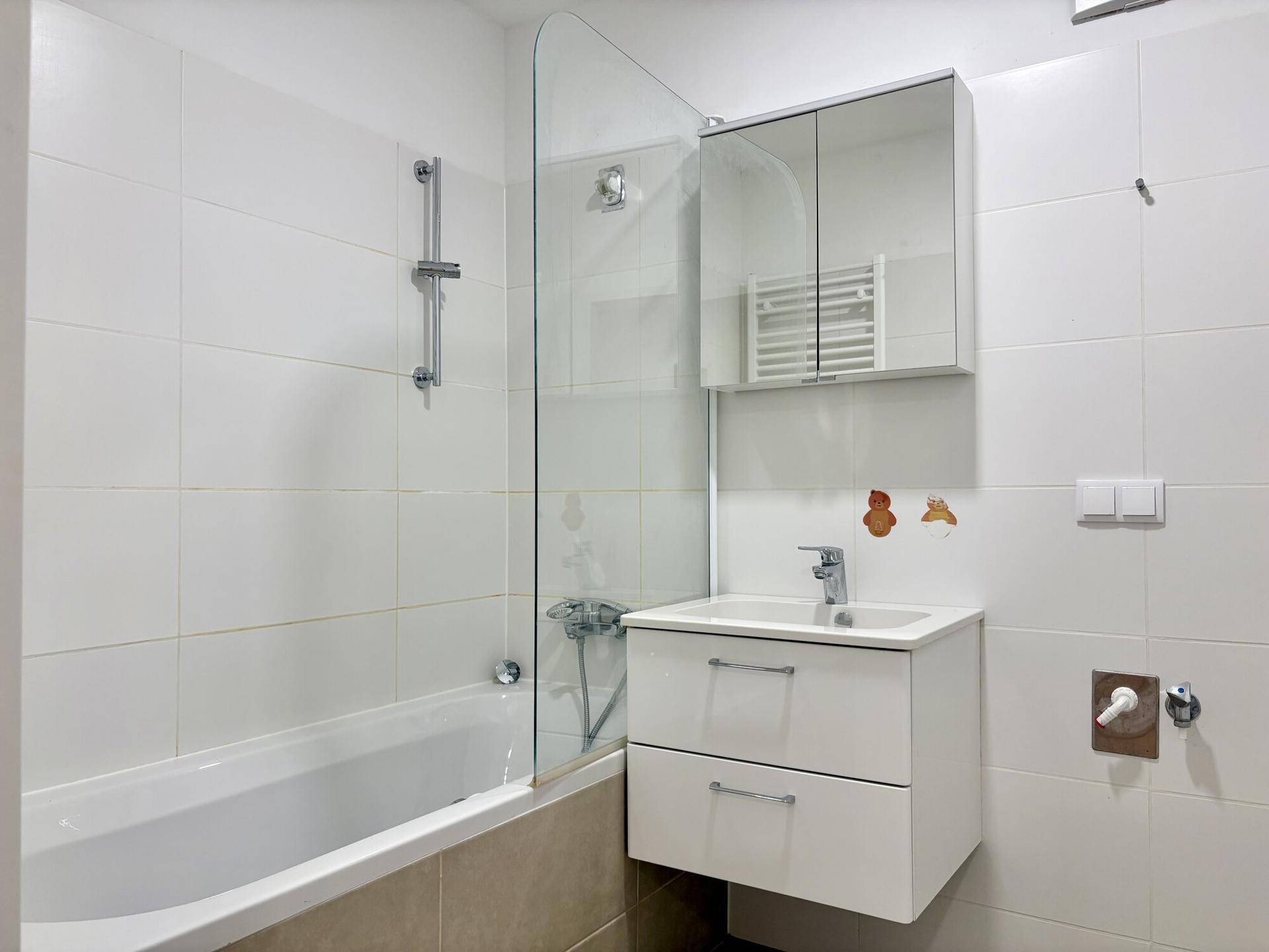 Modernes Badezimmer mit Badewanne, Duschwand, Einzelwaschbecken und Spiegelschrank.