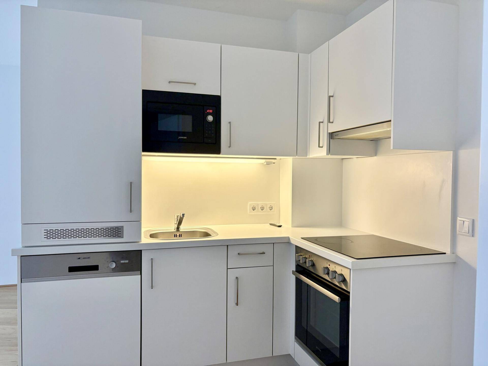 Moderne, kompakte Küchenzeile mit weißen Schränken, Induktionskochfeld, Backofen und Mikrowelle.