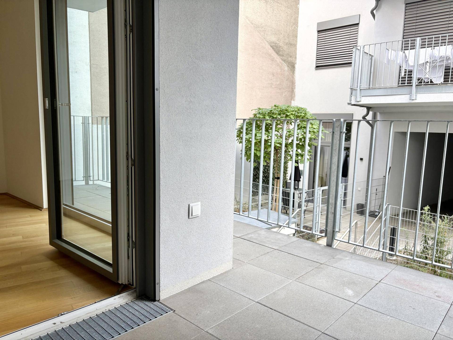 Balkon mit Fliesenboden und modernem Metallgeländer, bietet einen Blick auf den Innenhof.