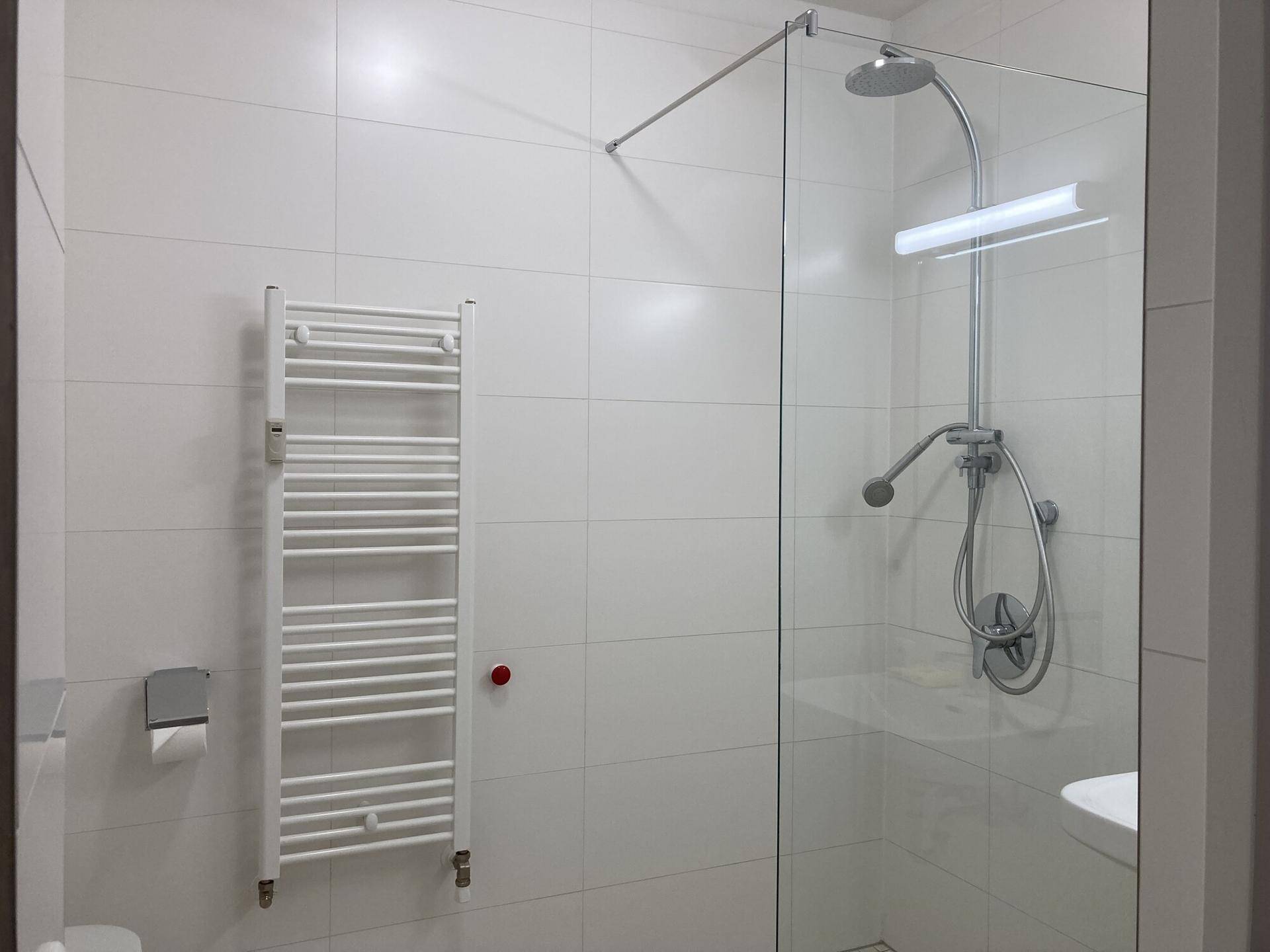Modernes Badezimmer mit weiß gefliesten Wänden, ebenerdiger Dusche und Handtuchheizkörper.