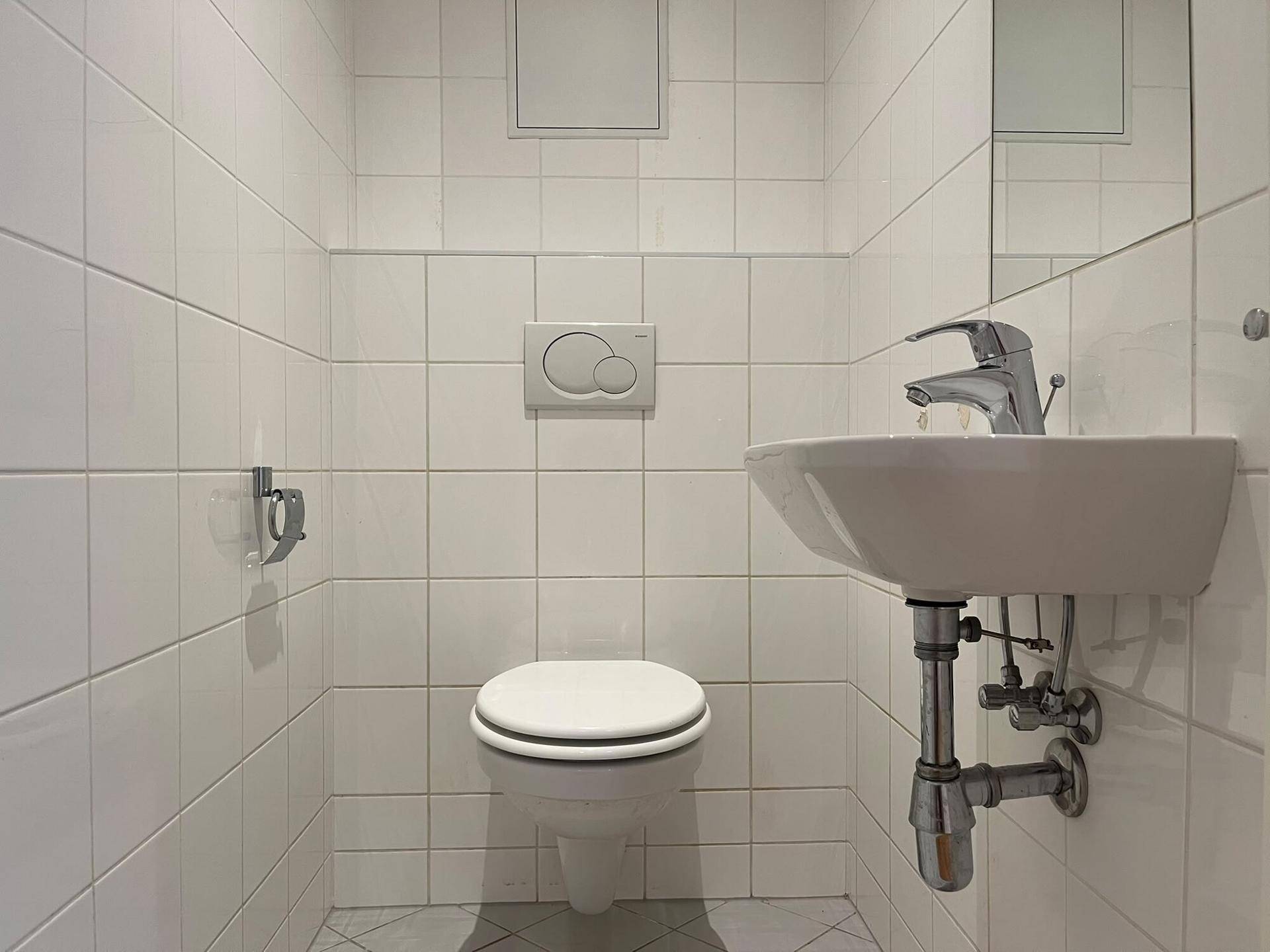 Kleines Gäste-WC mit wandhängender Toilette und einem kompakten Waschbecken, weiß gefliest.