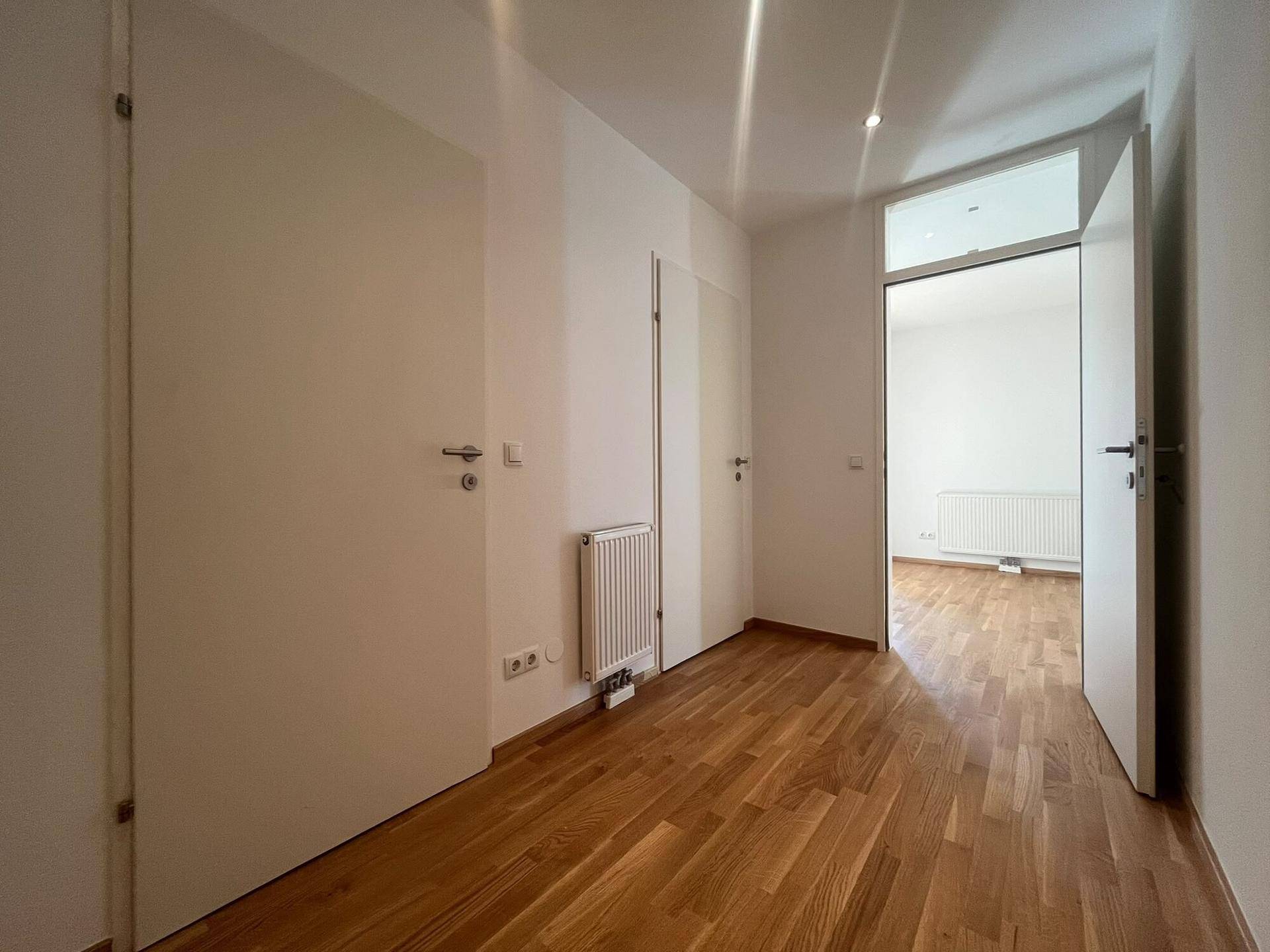 Heller Flur mit Holzboden und weißen Türen, der zu weiteren Räumen führt.
