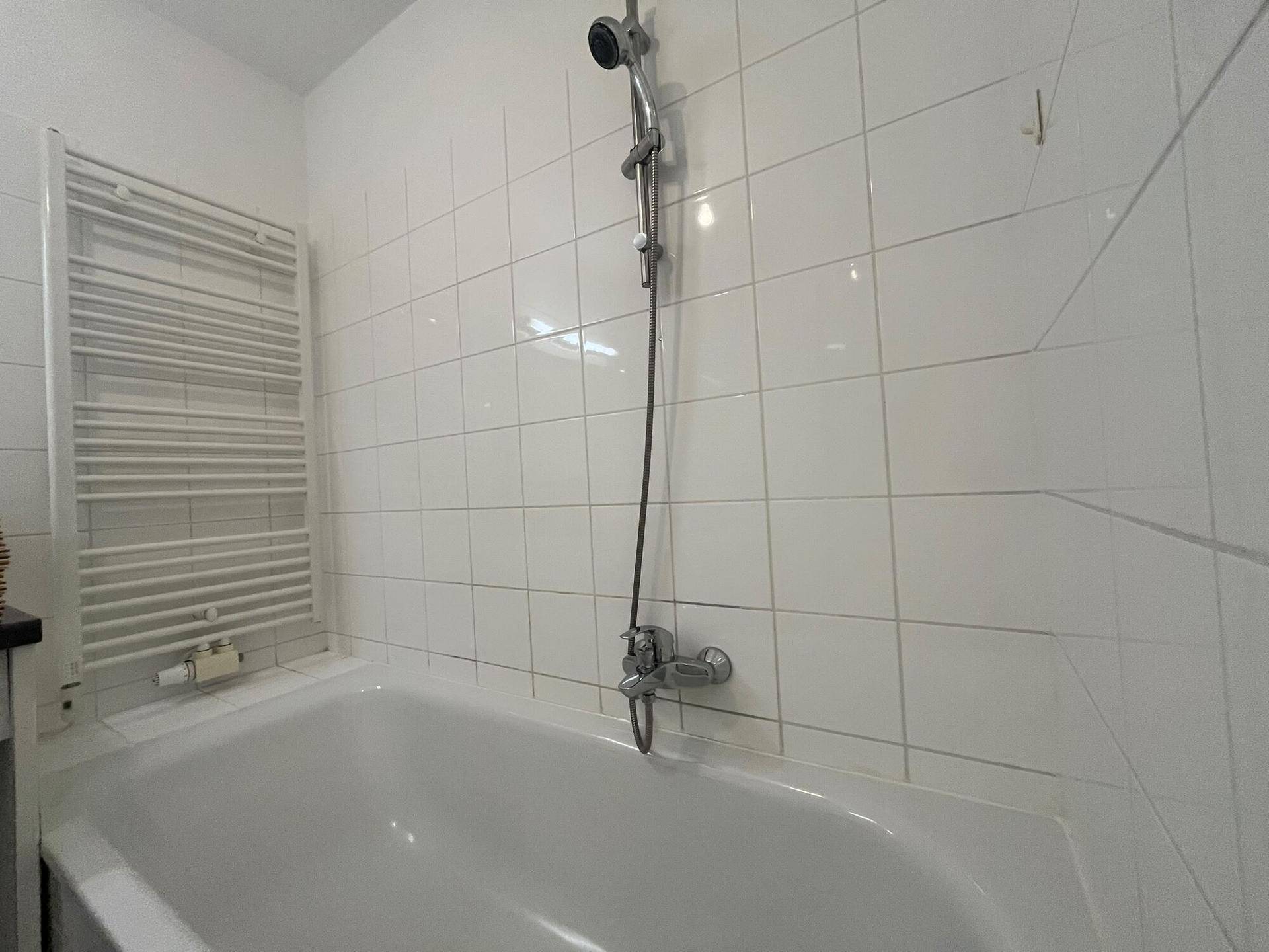 Badezimmer mit Badewanne und einem beheizten Handtuchhalter, vollständig weiß gefliest.