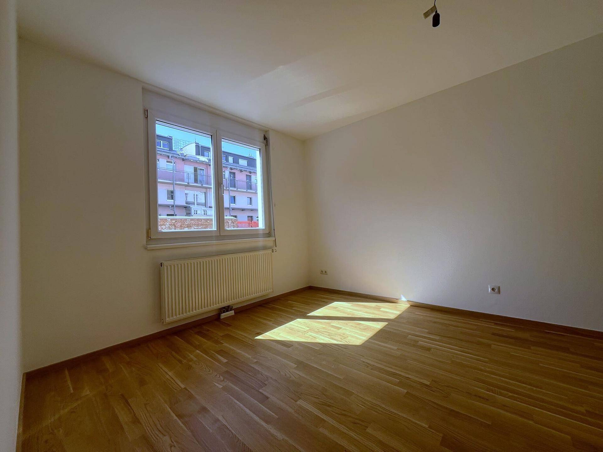 Schlafzimmer mit Holzboden und großem Fenster, das viel Tageslicht hereinlässt.