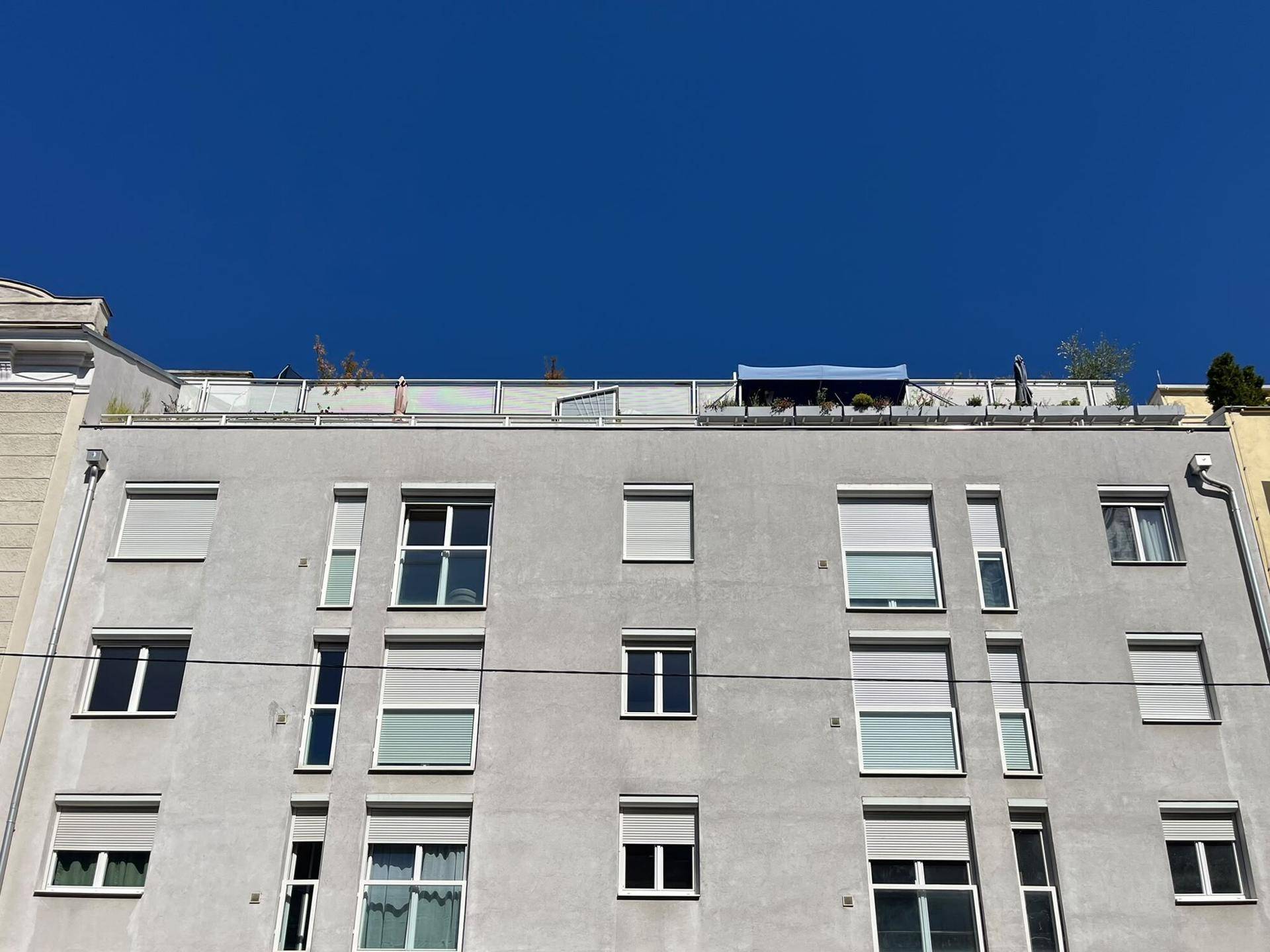 Moderne Gebäudefassade mit zahlreichen Fenstern und einer Dachterrasse im oberen Bereich.