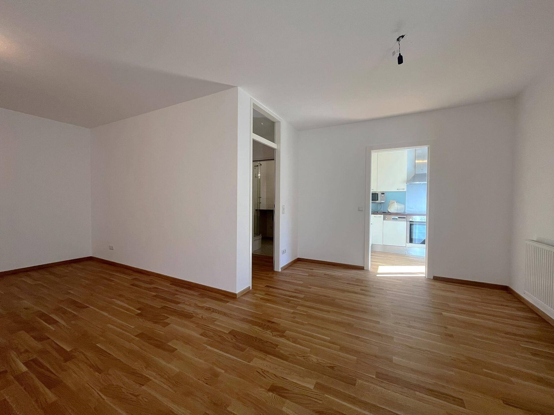 Geräumiges Wohnzimmer mit hellem Holzboden und Zugang zur angrenzenden Küche.