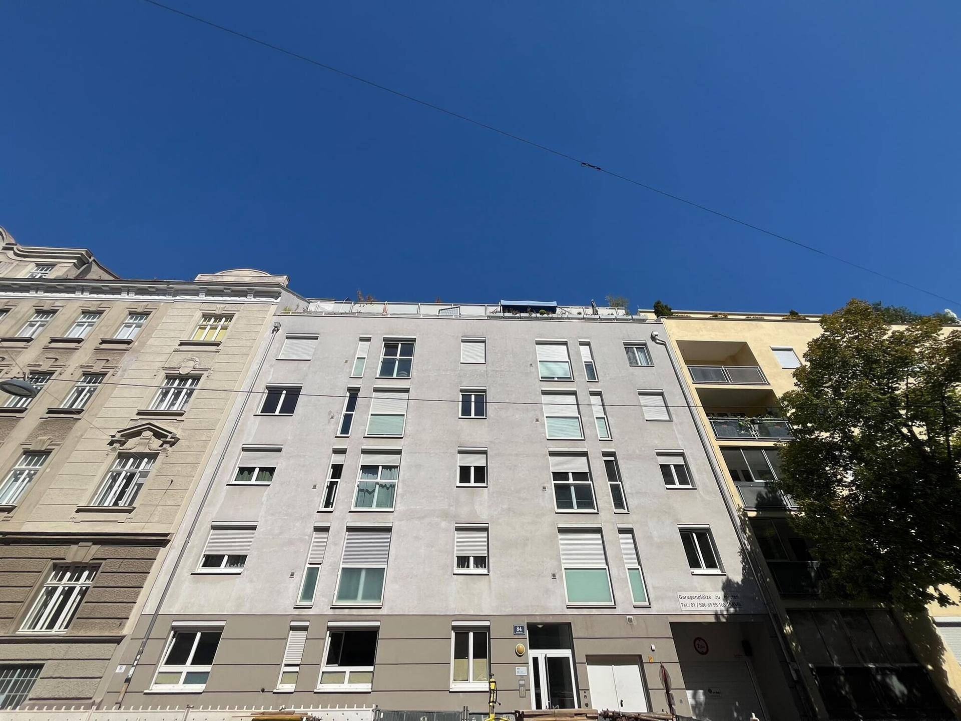 Gesamtansicht der modernen Gebäudefassade mit angrenzenden Altbauten unter blauem Himmel.