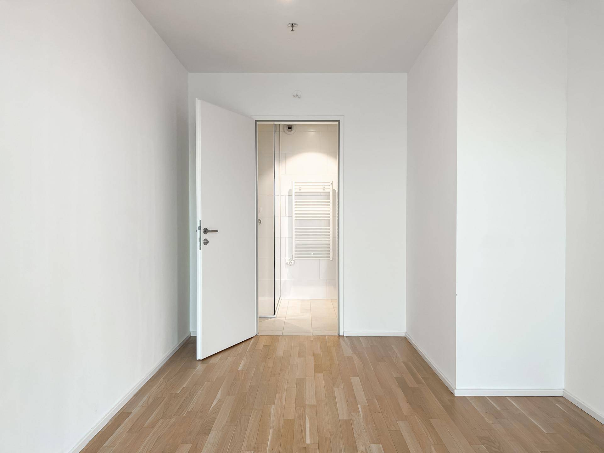 Leeres Zimmer mit Parkettboden und direktem Zugang zu einem gefliesten Badezimmer.