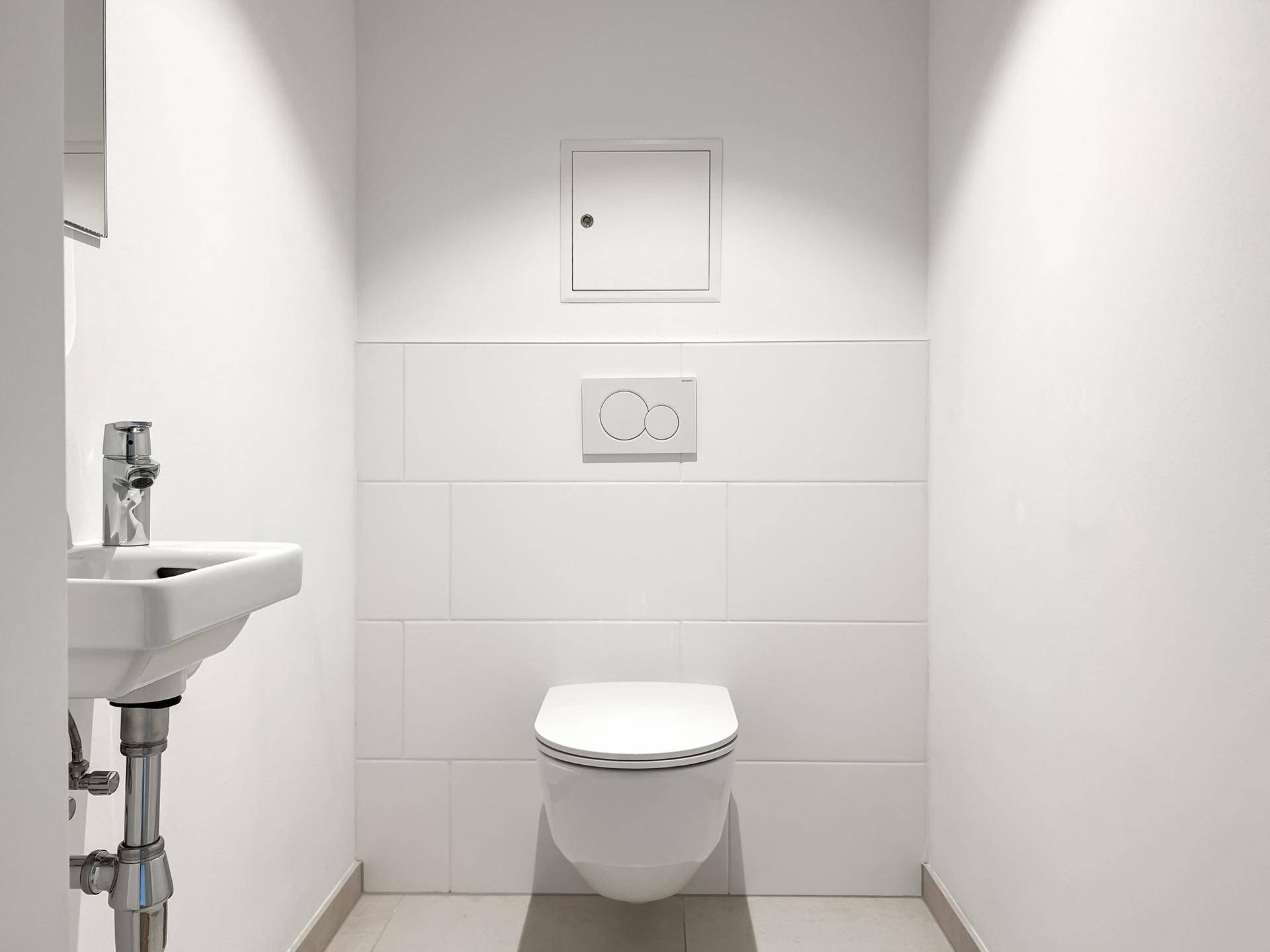 Separates WC mit wandhängender Toilette und kleinem Handwaschbecken.
