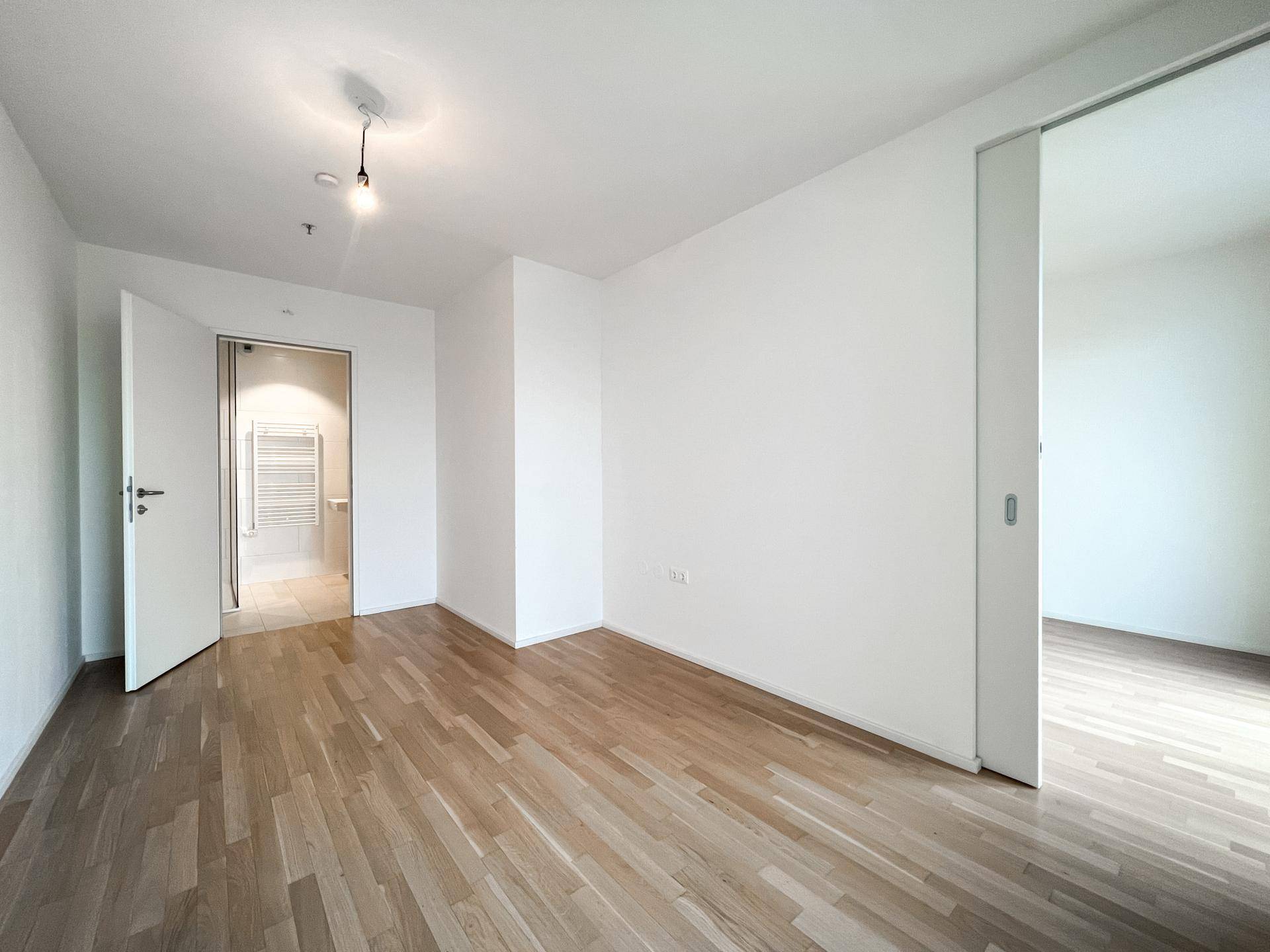 Helles Zimmer mit Holzboden und Zugang zu einem modernen Badezimmer.