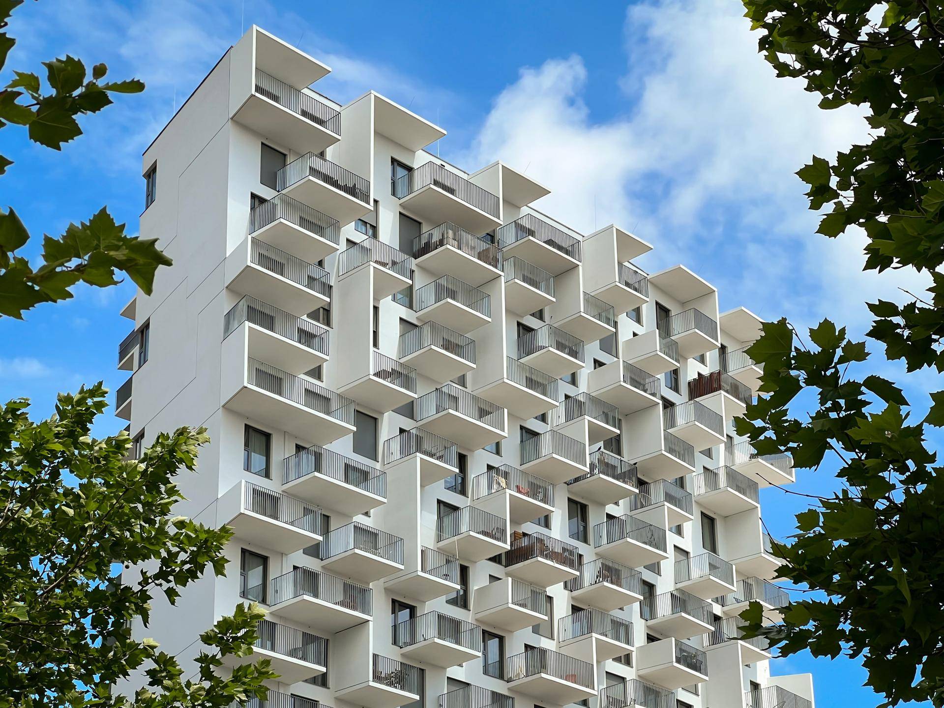Detailansicht der modernen Fassade mit vielen versetzten Balkonen unter blauem Himmel.