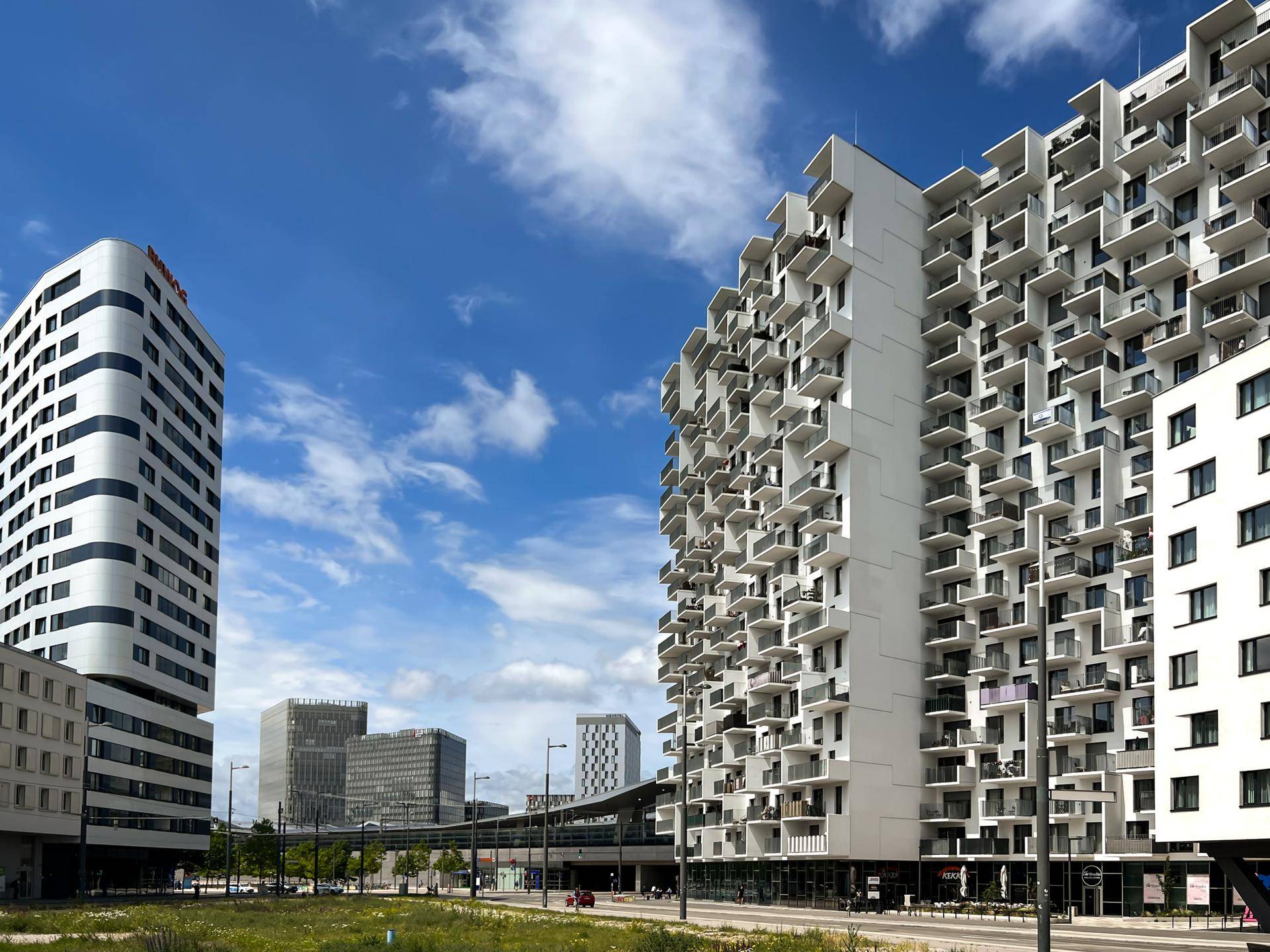 Stadtansicht mit modernen Wohngebäuden und urbaner Infrastruktur unter blauem Himmel.
