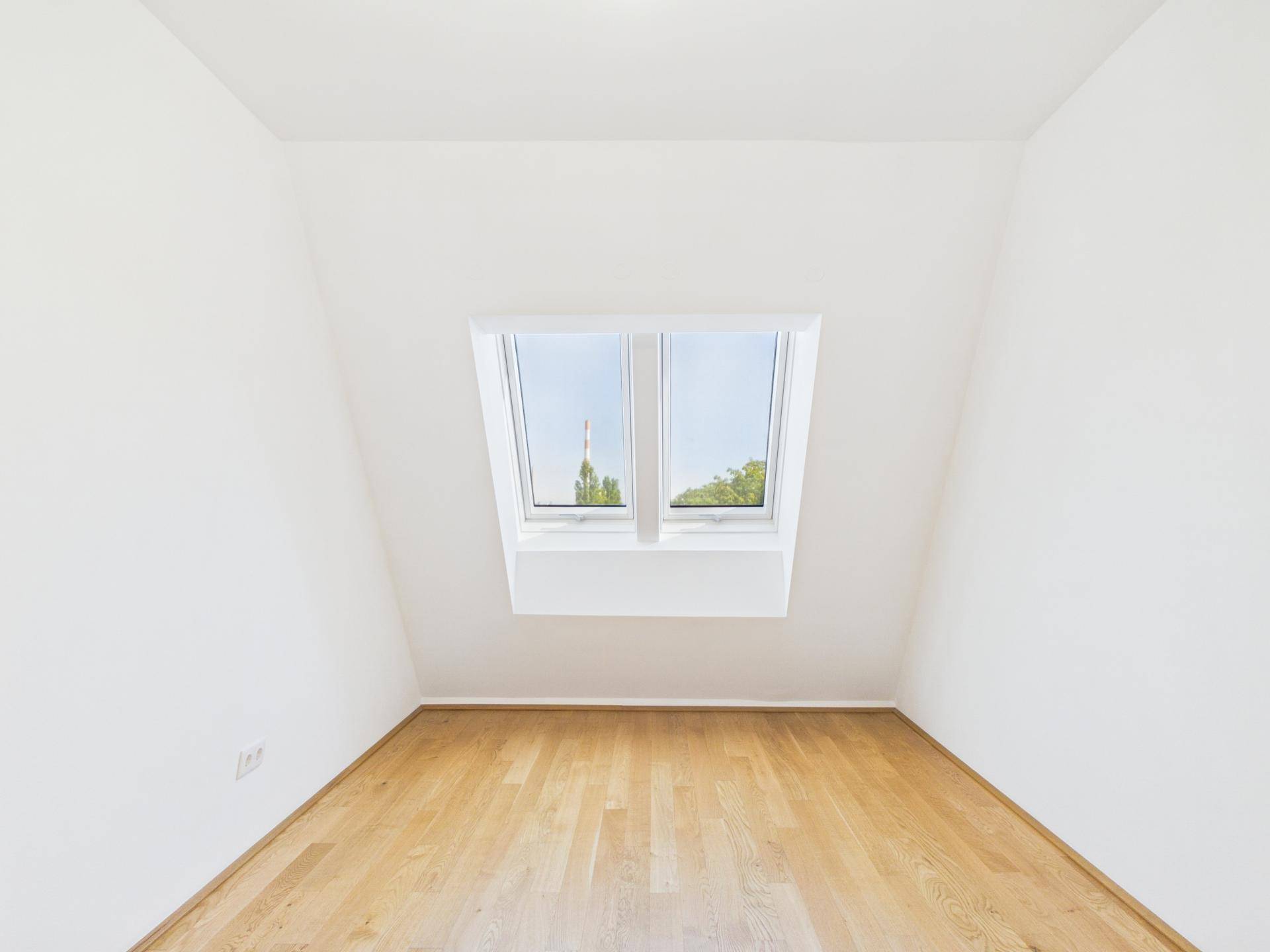 Helles Zimmer mit Holzboden, weißen Wänden und einem großen Dachfenster.