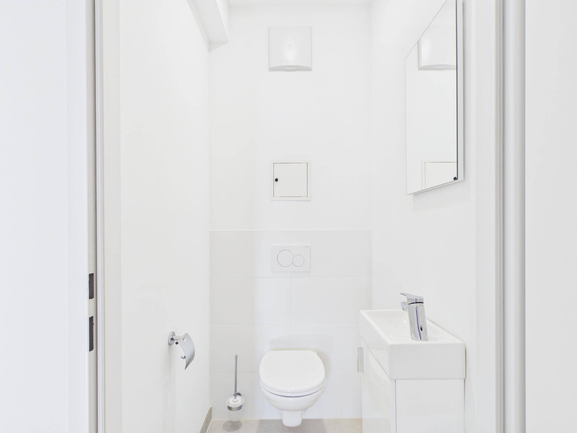 Modernes Gäste-WC mit wandhängender Toilette, kleinem Waschbecken und Spiegel.