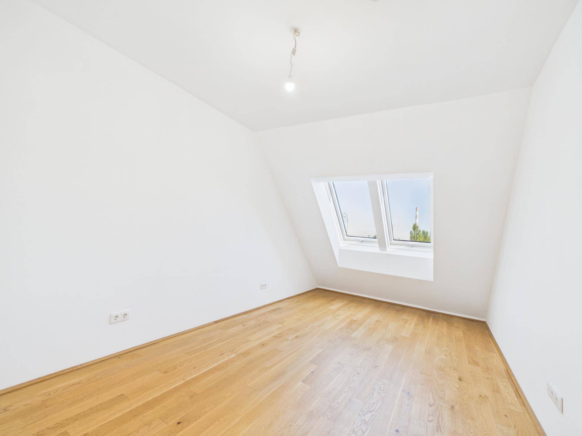 Helles Zimmer mit Holzboden, weißen Wänden und einem großen Dachfenster.