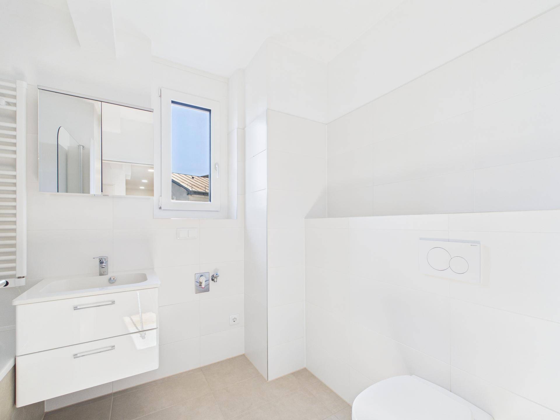 Modernes Badezimmer mit Toilette, Waschbecken, Spiegelschrank und Fenster für Tageslicht.