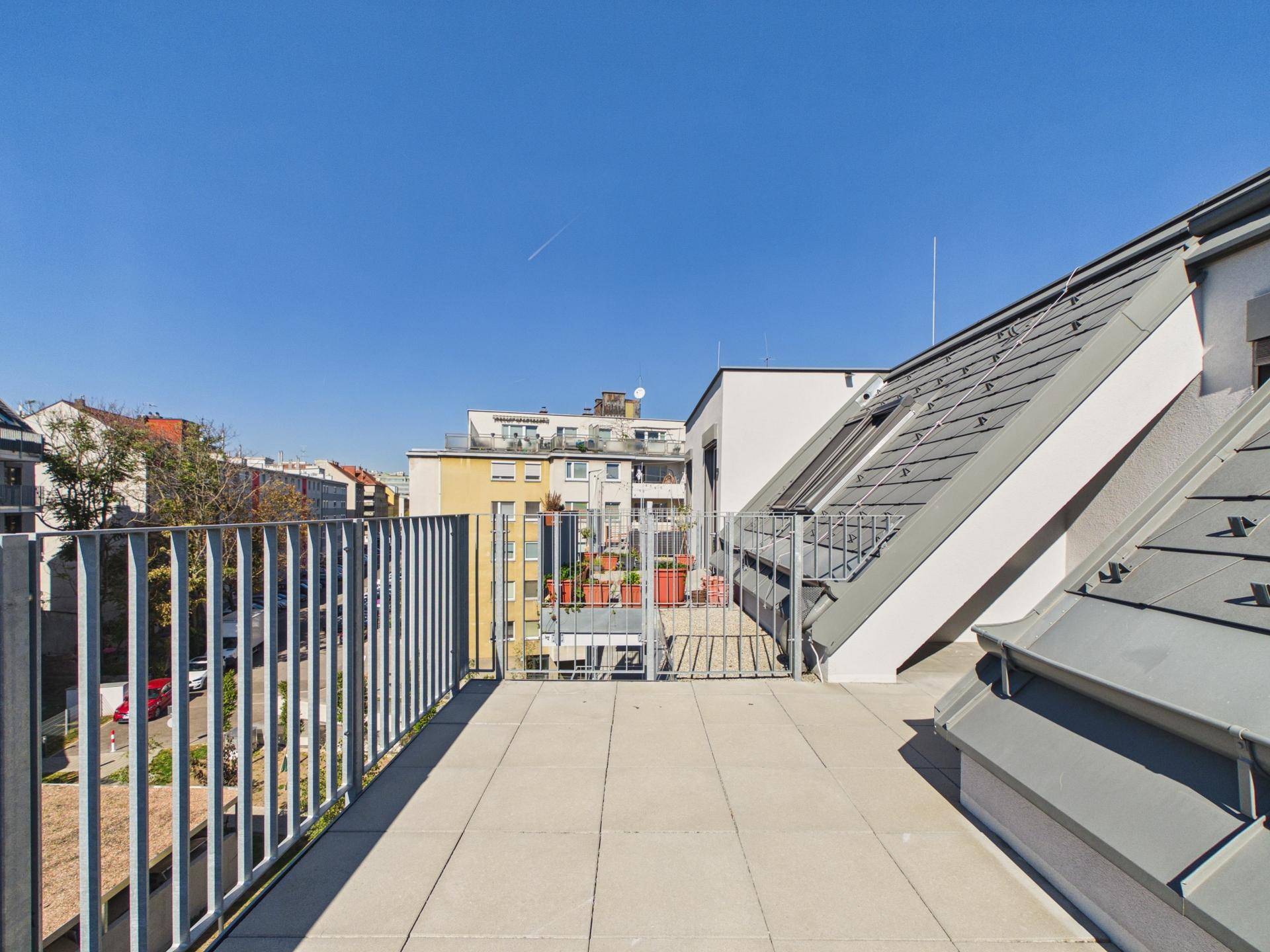 Geräumige Dachterrasse mit Fliesenboden und Blick auf die umliegenden Gebäude.