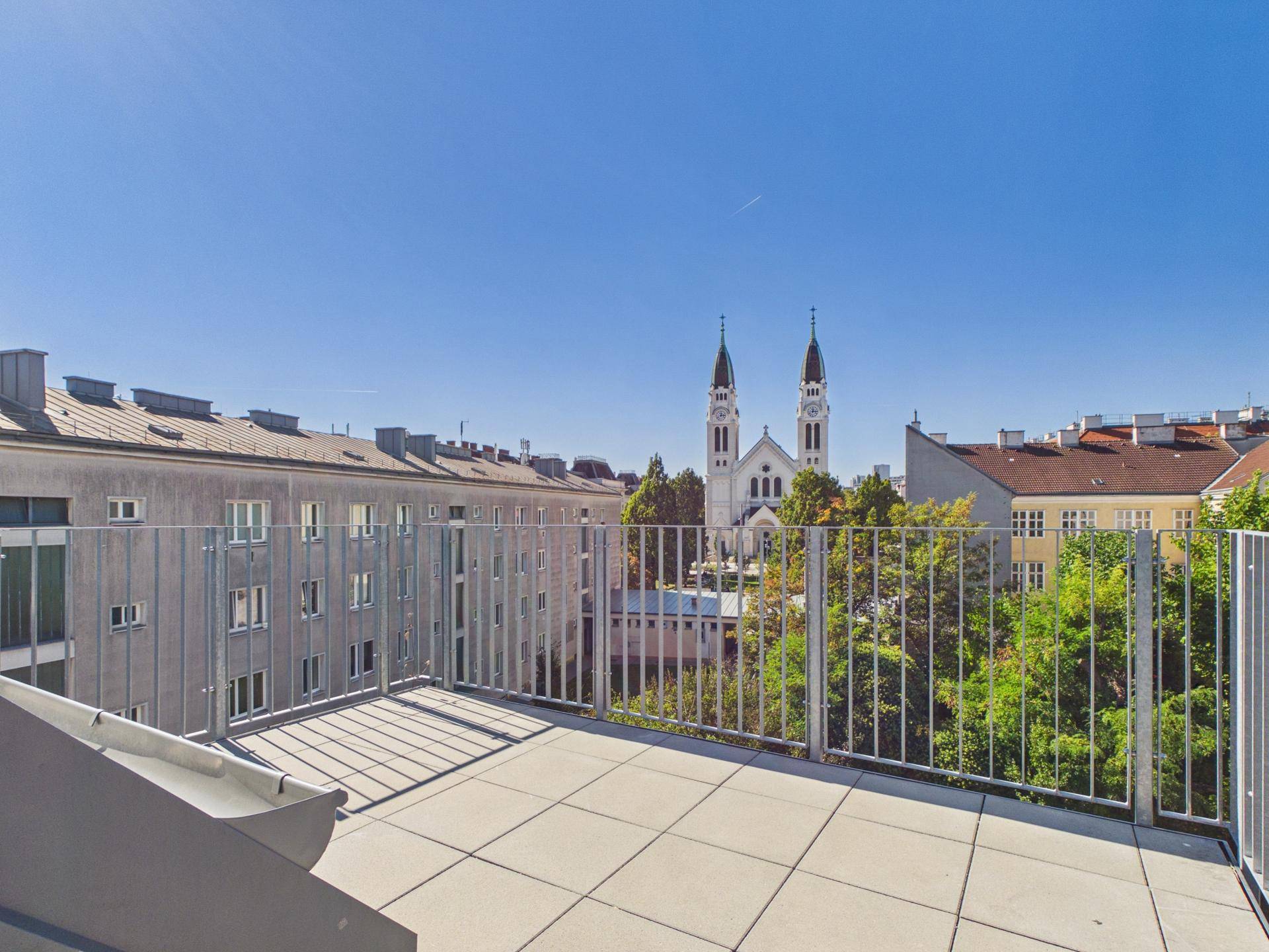 Sonniger Terrassenbereich mit weitem Blick auf die Stadt und eine markante Kirche.