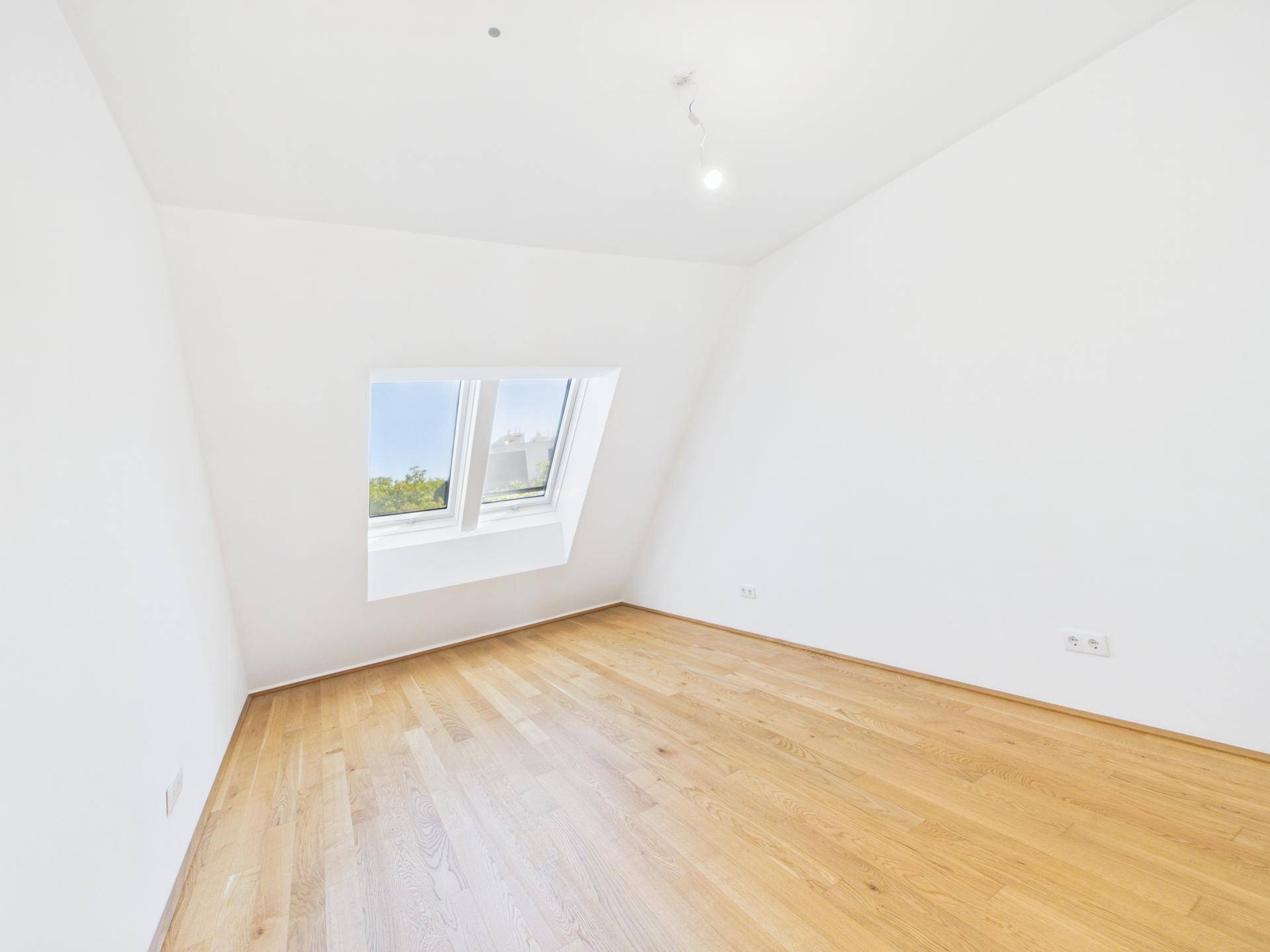 Helles Zimmer mit Holzboden, weißen Wänden und einem großen Dachfenster.