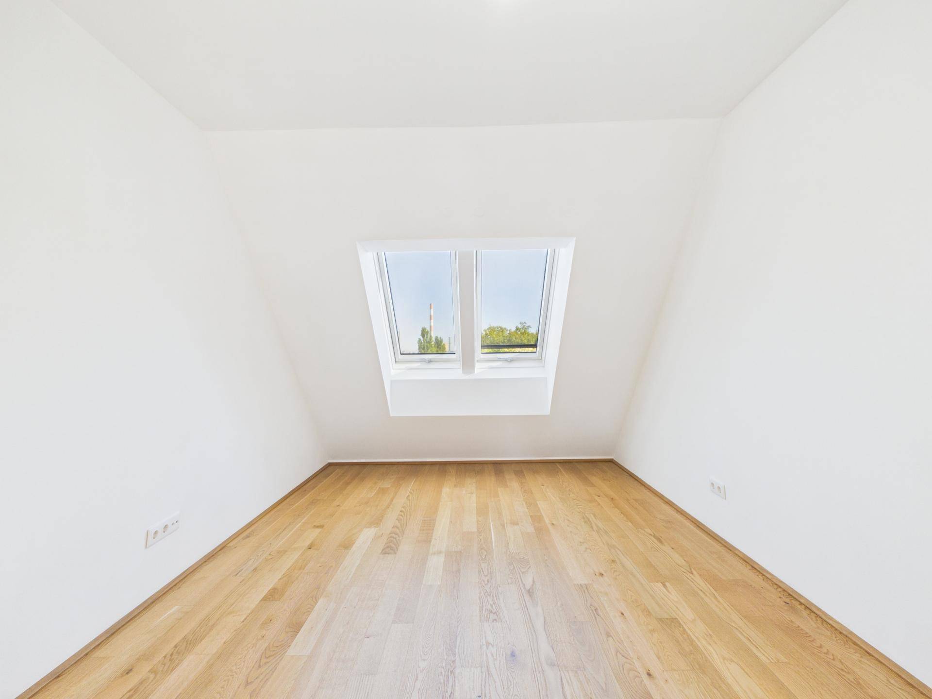 Helles Zimmer mit Holzboden, weißen Wänden und einem großen Dachfenster.