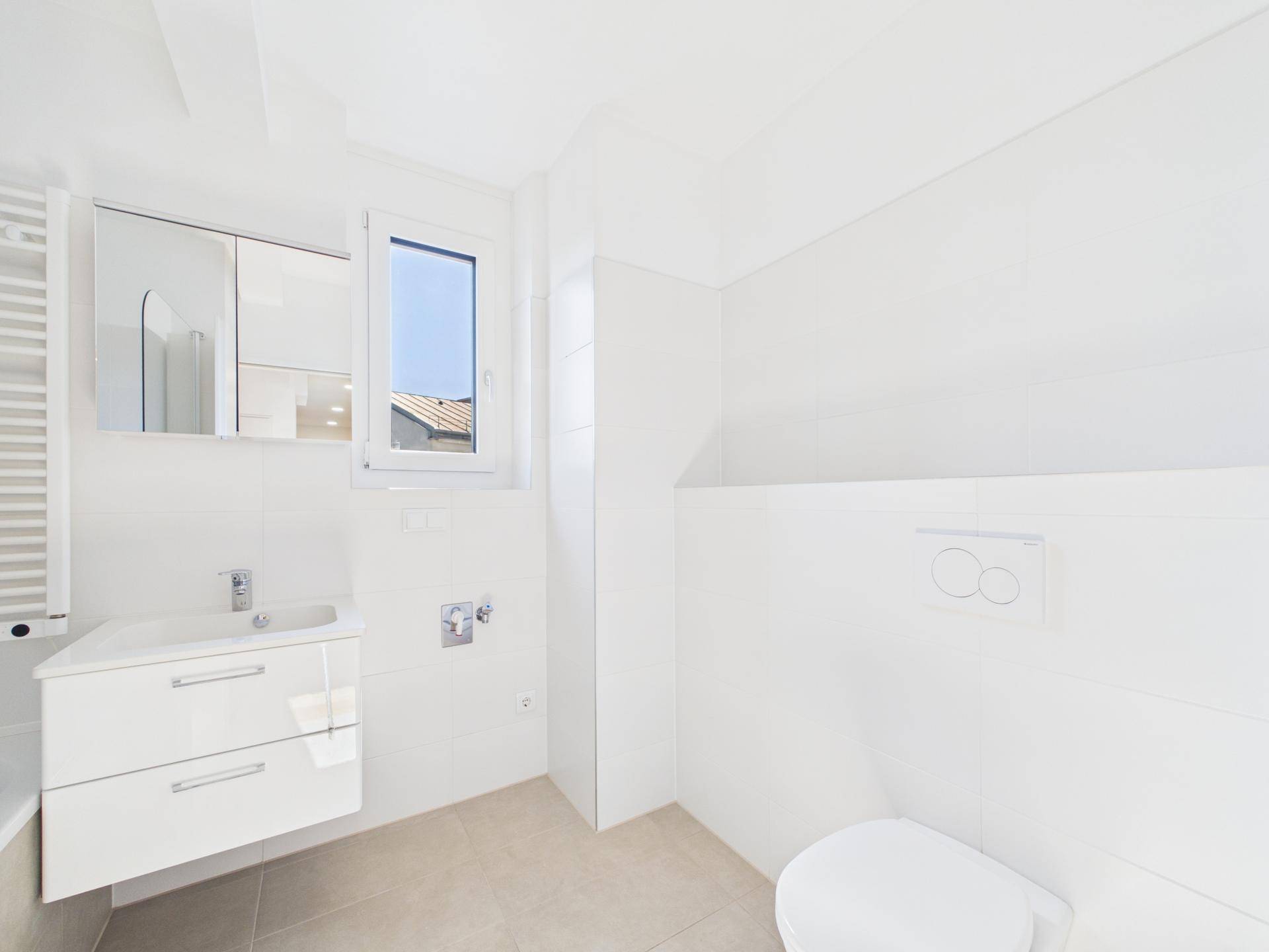 Modernes Badezimmer mit Toilette, Waschbecken, Spiegelschrank und Fenster für Tageslicht.