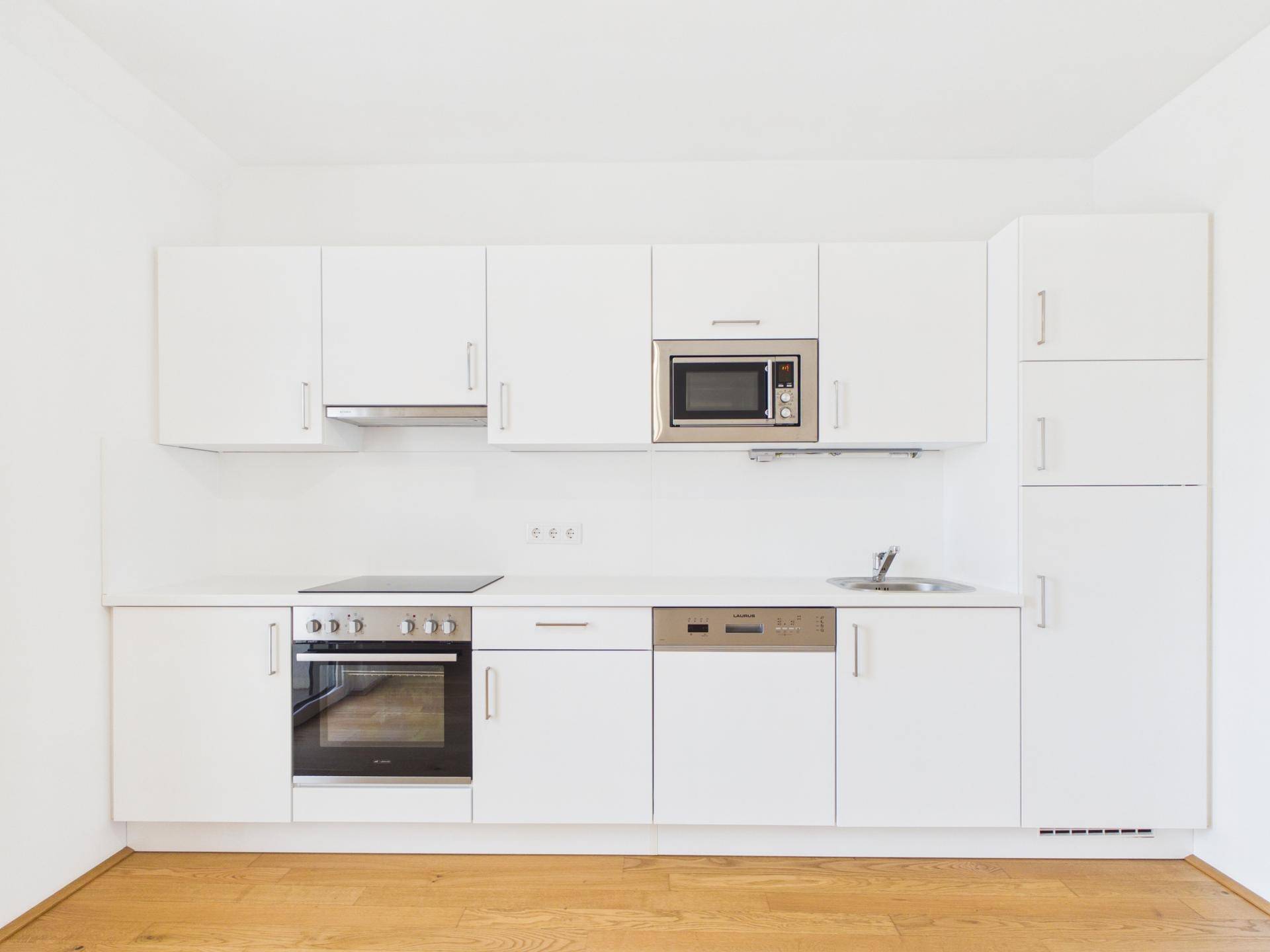 Moderne Einbauküche in Weiß mit integrierten Geräten wie Backofen, Mikrowelle und Geschirrspüler.