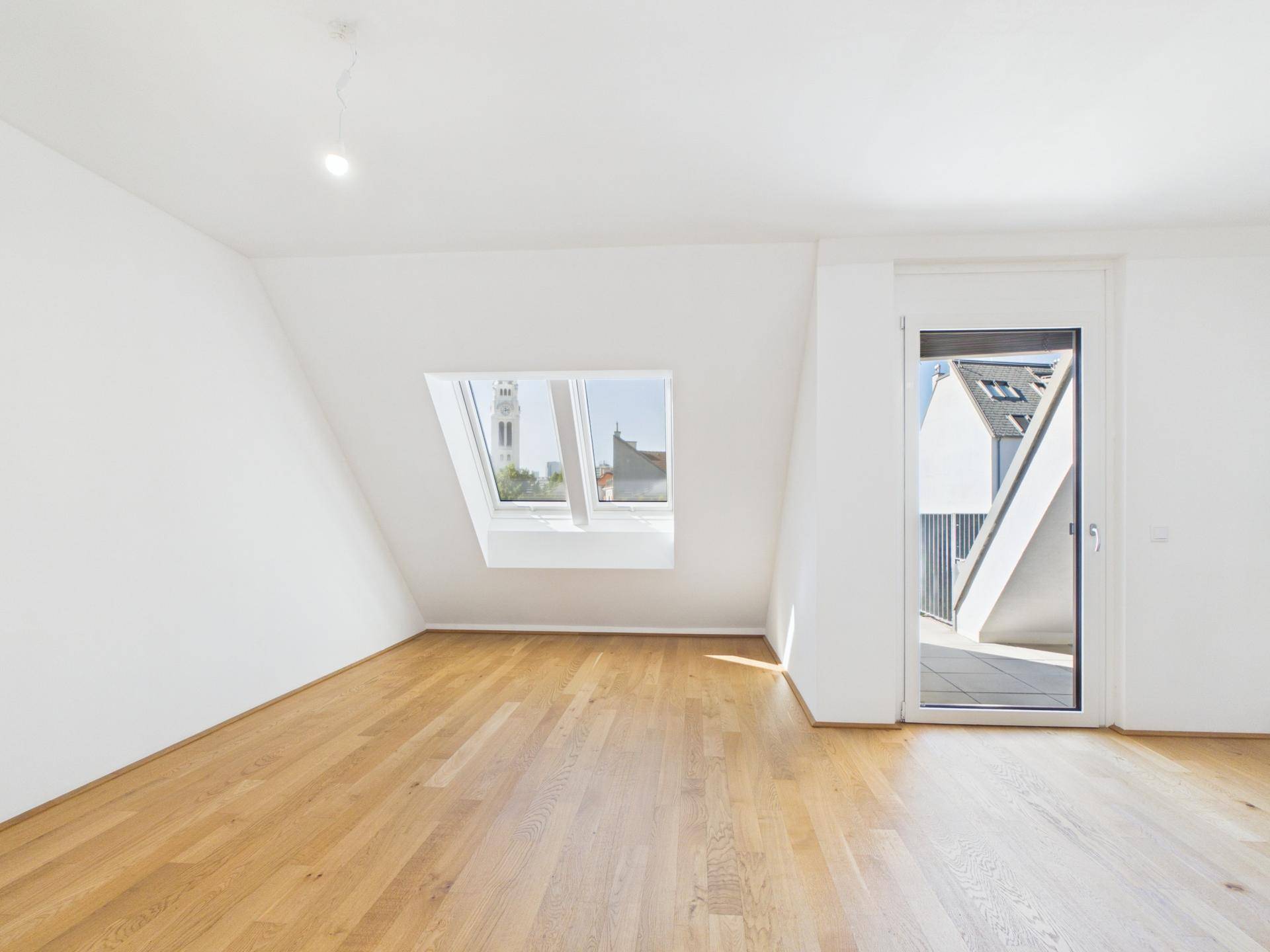 Helles Zimmer mit Holzboden, Dachfenster mit Kirchturmblick und Zugang zur Terrasse.