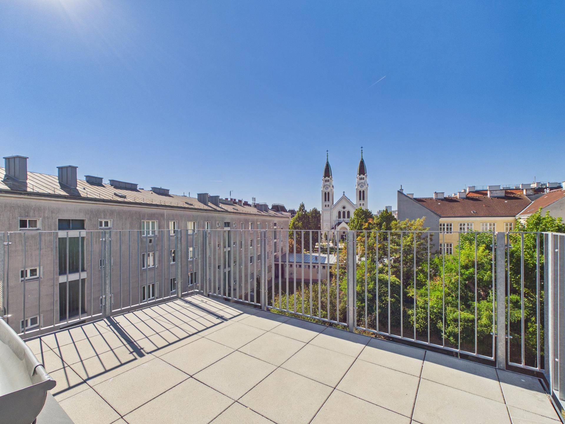 Sonniger Terrassenbereich mit weitem Blick auf die Stadt und eine markante Kirche.