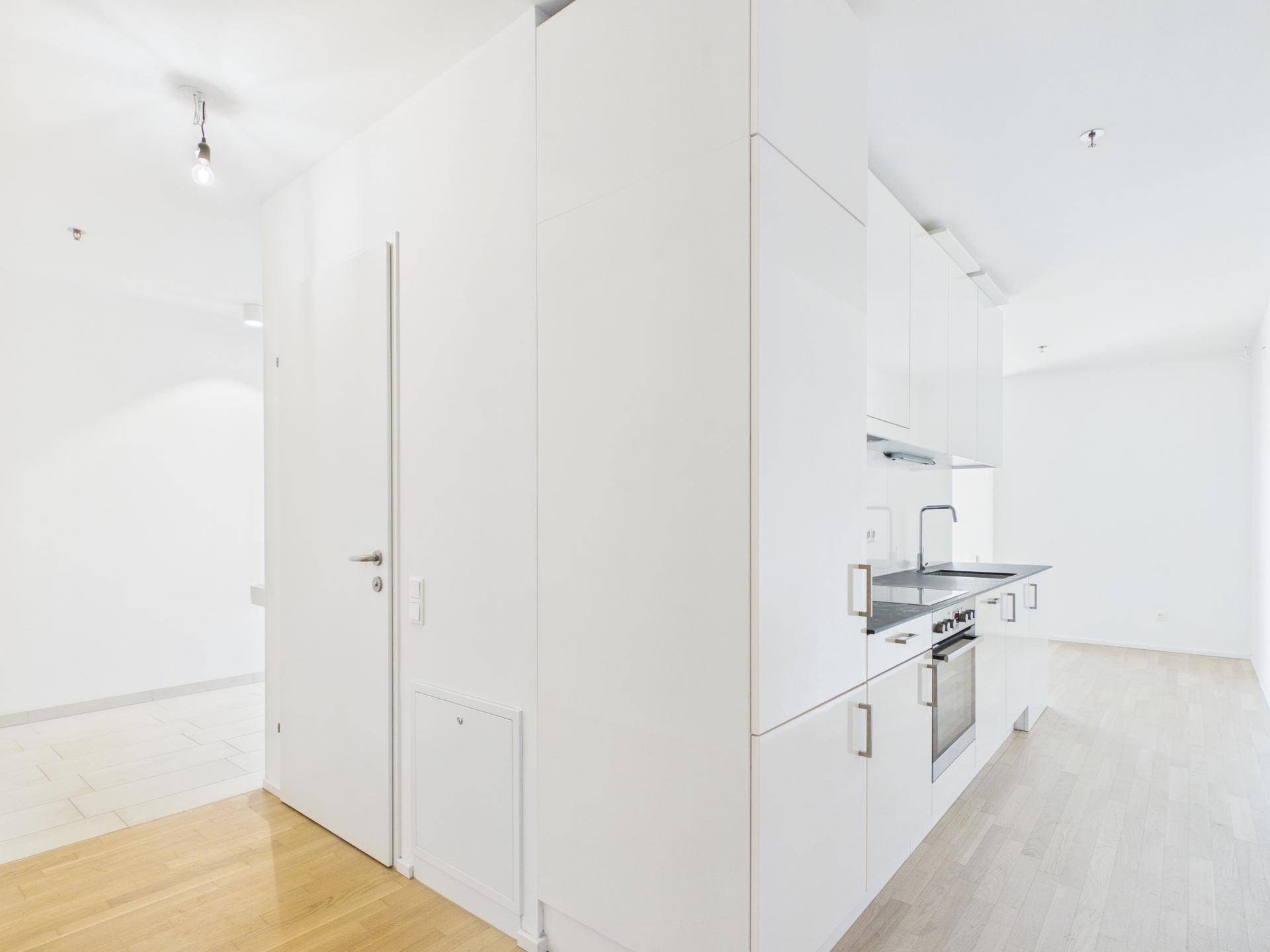 Helle, moderne Küchenzeile mit weißen Fronten, integrierten Geräten und Holzfußboden.