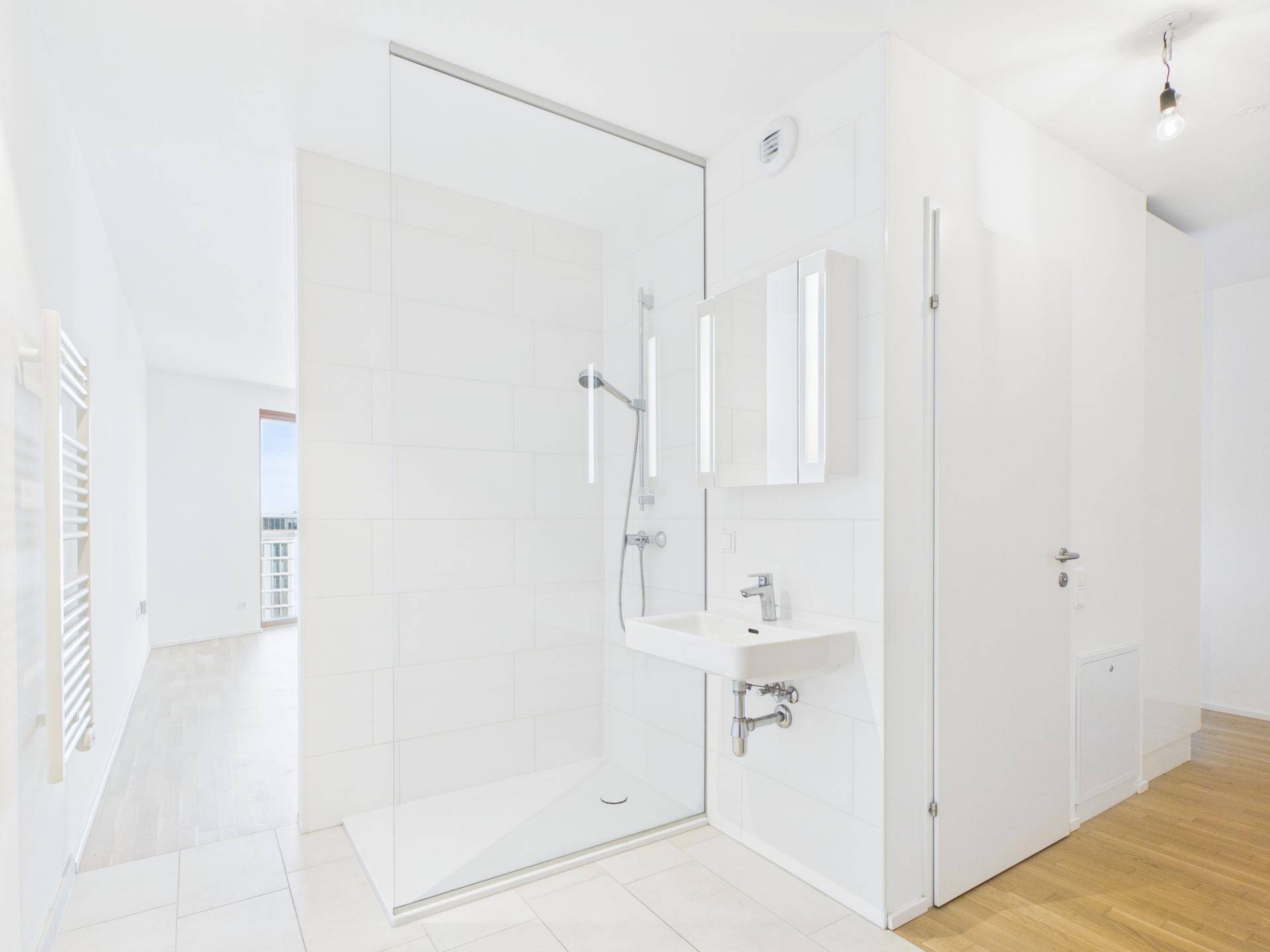 Modernes Badezimmer mit großer begehbarer Dusche, weiß gefliest und mit kleinem Waschbecken.