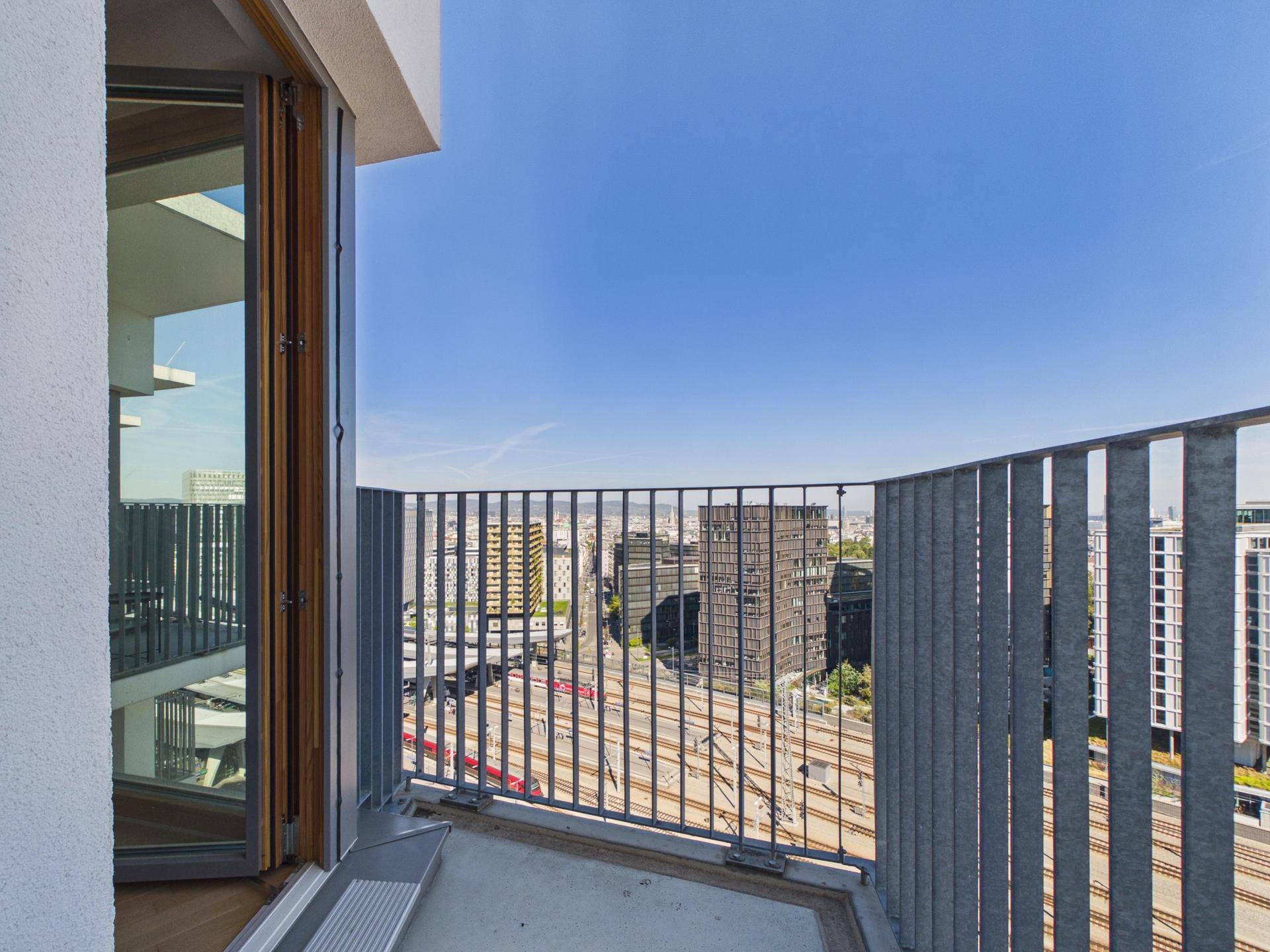 Balkon mit Metallgeländer und weitem Blick über die Stadt und Bahngleise.