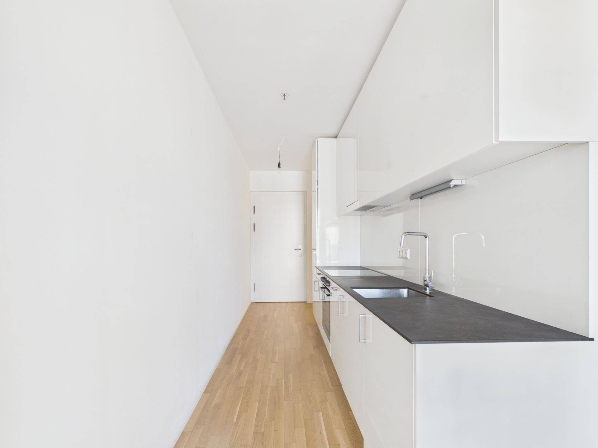Moderne, schmale Küche mit weißen Hochglanzschränken, dunkler Arbeitsplatte und Holzboden.