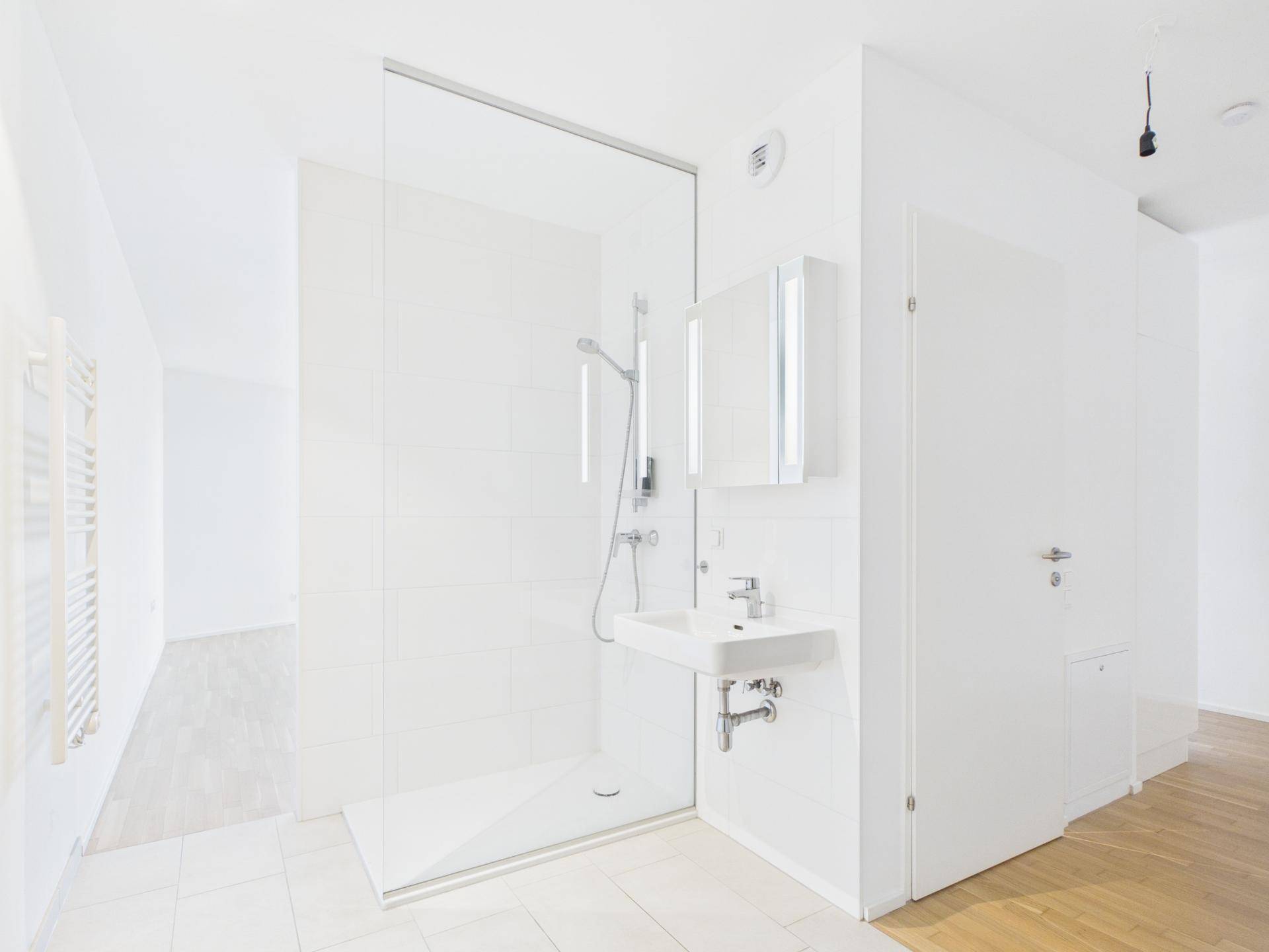 Modernes Badezimmer mit ebenerdiger Dusche, weißem Waschbecken und Spiegelschrank.