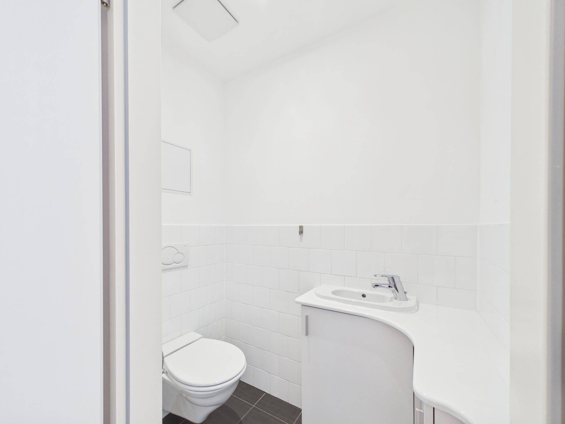 Kleines Gäste-WC mit weißen Fliesen, wandhängendem WC und einem kompakten Waschbecken.