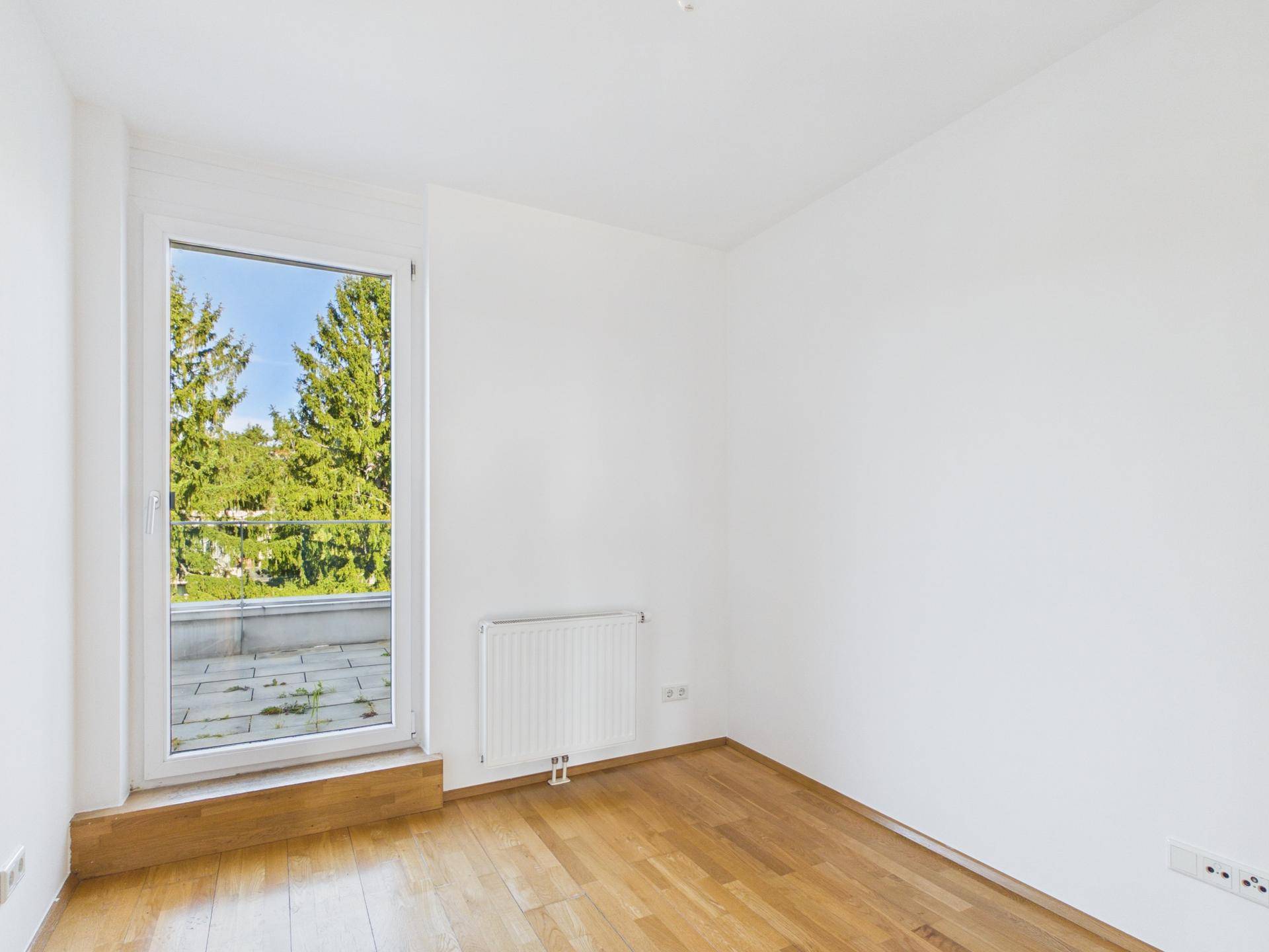 Helles Schlafzimmer mit Holzboden, weißen Wänden und Zugang zu einer Terrasse mit Grünblick.