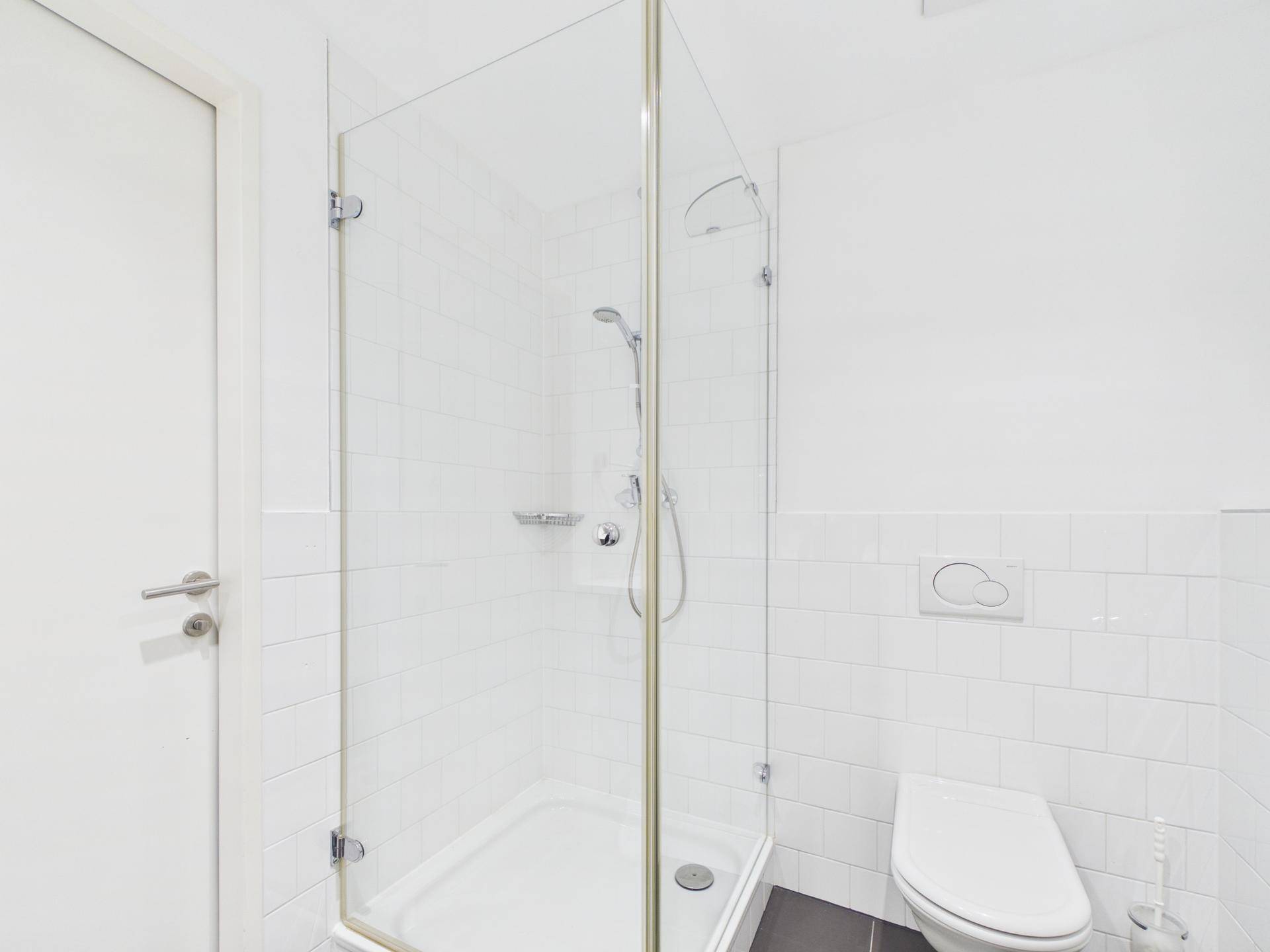 Helles Badezimmer mit Duschkabine, WC und weißen Fliesen.